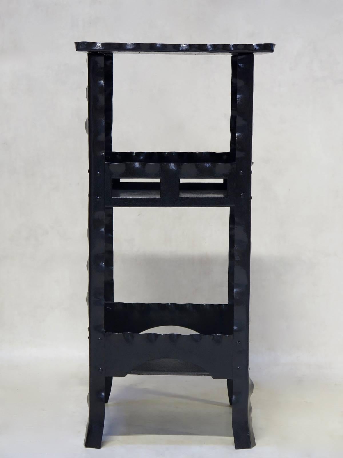 Folk-art pedestal with three tiers, made of iron with scalloped edging and pretty cutout detailing. Painted black.