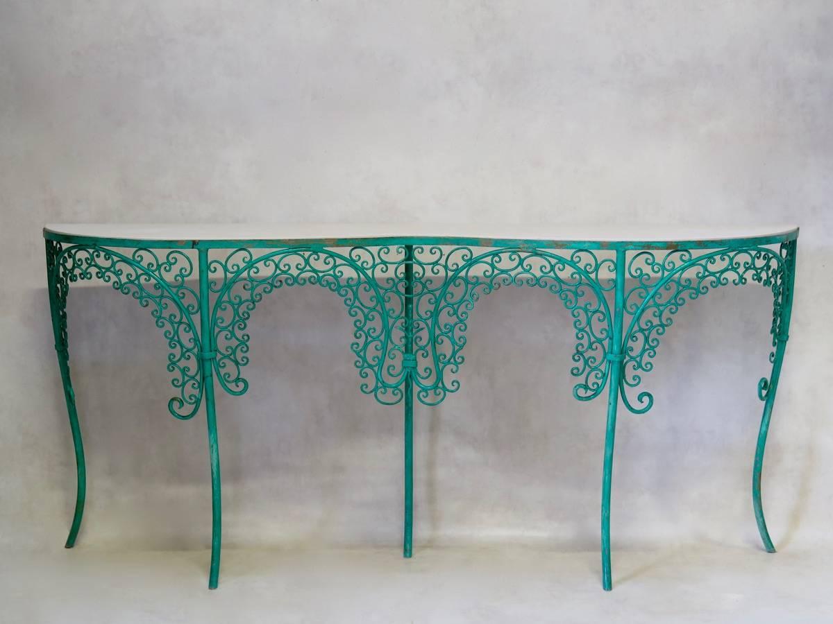 Elegant iron patio set comprising a console, a coffee table, two chairs, a settee and two curule stools.
The set presents delicate fretwork and hammered iron, and is painted in its original green colour. 
The console has a curved front, with