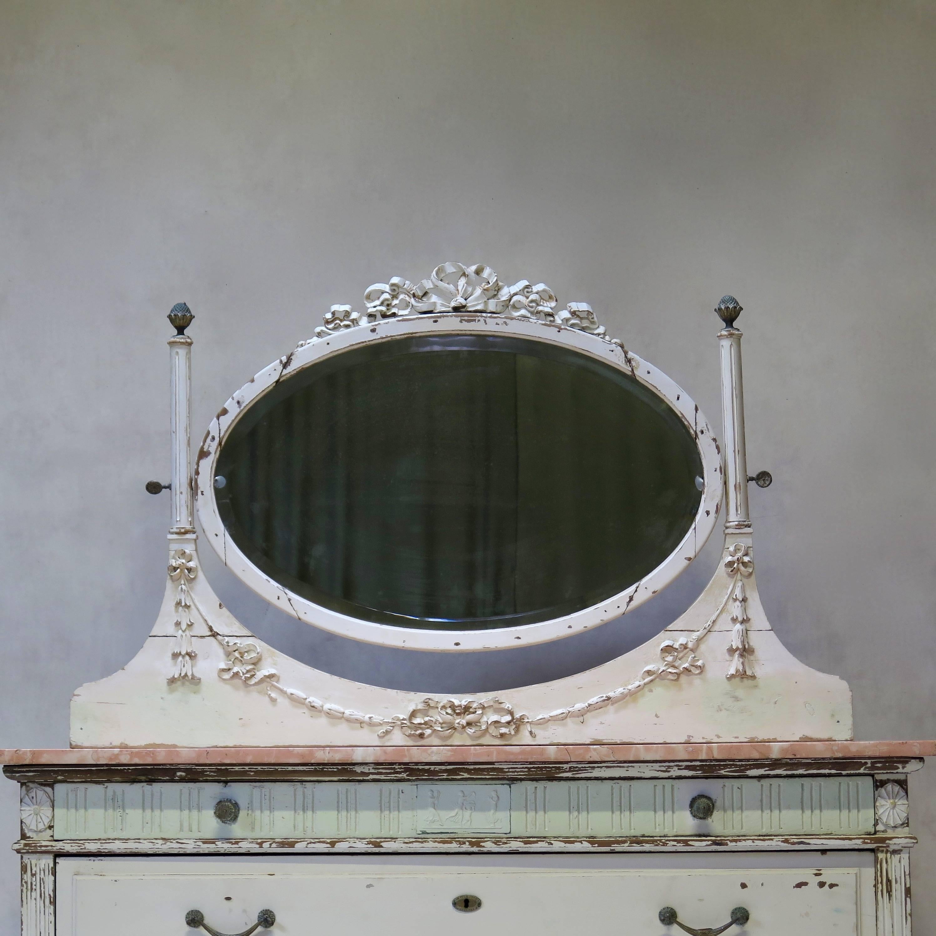 Louis XVI style chest of drawers topped with a slab of pink marble veined with white. 
The elegant oval mirror above is original, with a beveled edge, and its angle can be adjusted by turning the two brass rosettes at either side. The mirror is