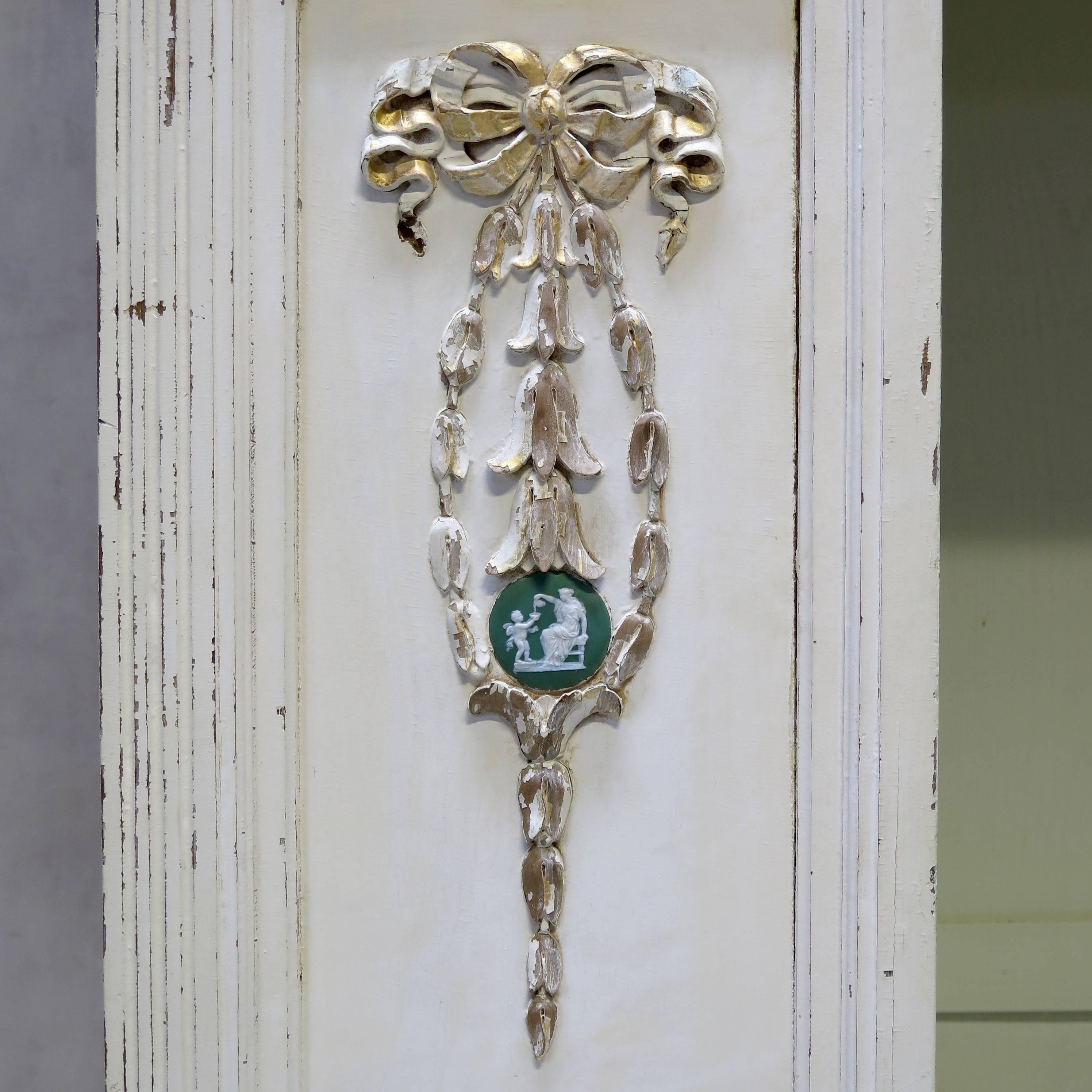 Elegant Louis XVI style wardrobe. The door is fitted with a beveled oval full-length mirror. The sections on either side of the door are decorated with carved bow and ribbon motifs and Wedgwood cameos. At the top is a mauve frosted glass section.