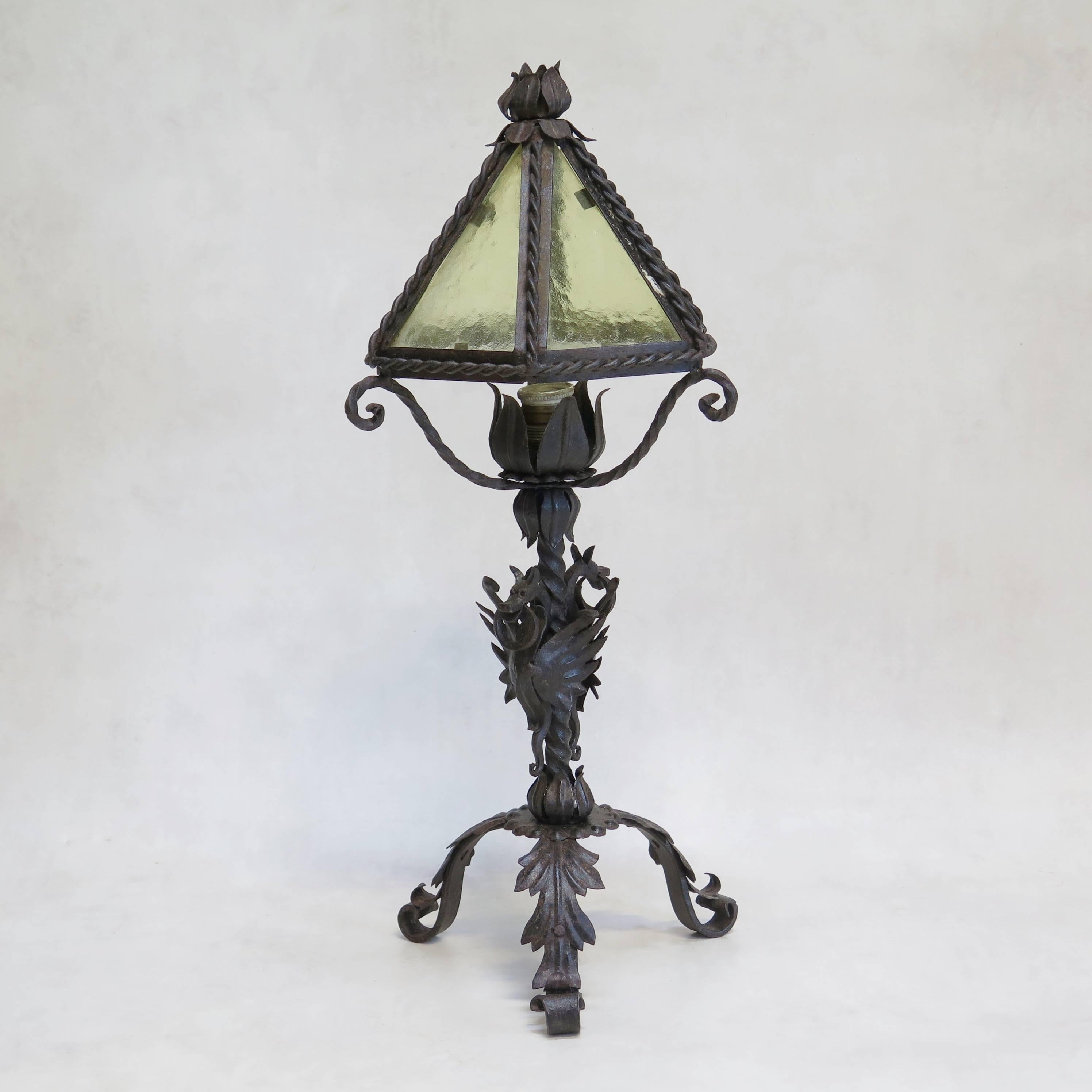 Ornate and lovely wrought-iron desk lamp complete with original lamp shade with yellow frosted glass panes. The base features two dragons with rings in their mouth. Mounted on a tripod base wit acanthus leaf detail.