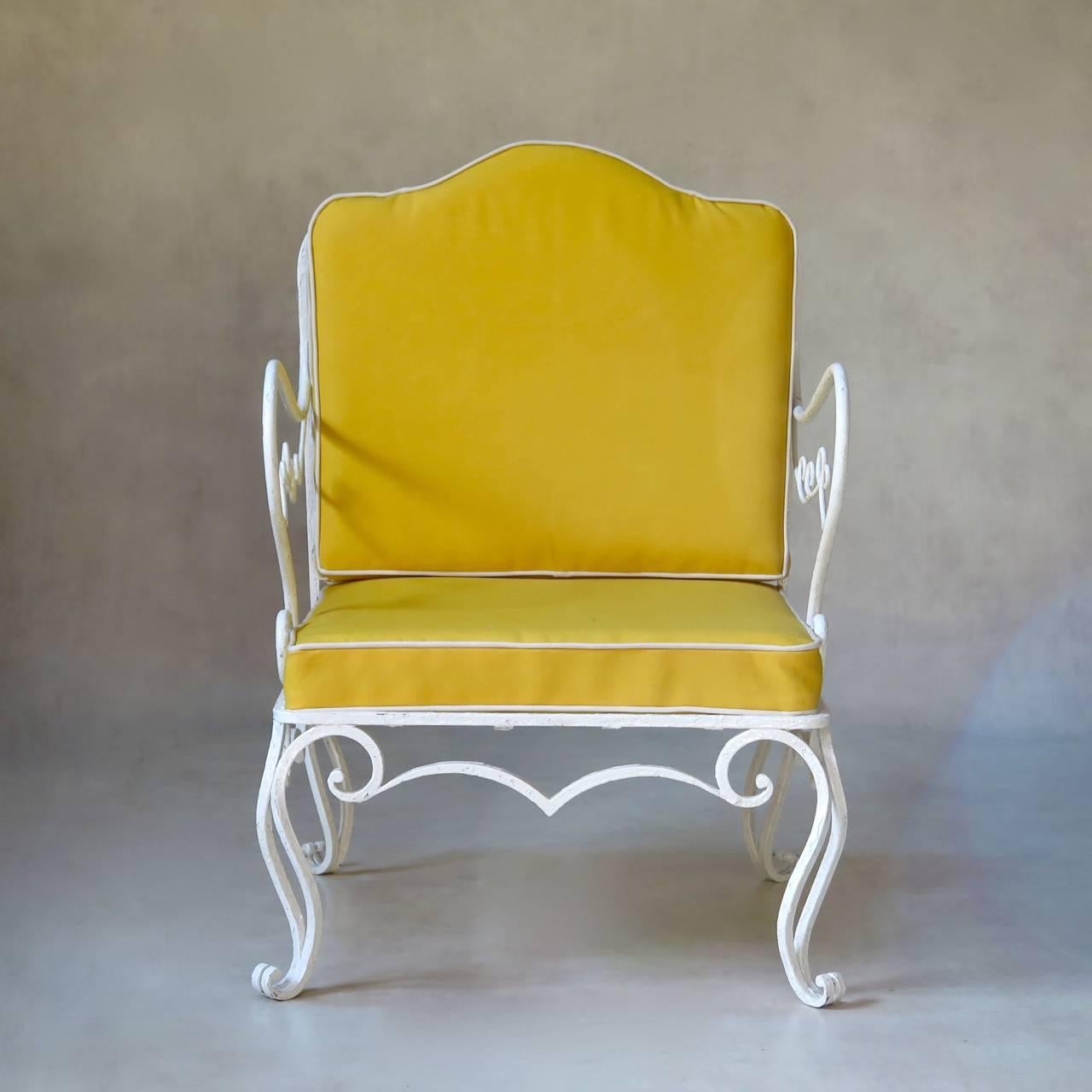 Very lovely and comfortable pair of wrought iron armchairs of elegant design. The backs and arms feature curlicue motifs. Raised on cabriole legs ending in scrolled feet. The seat and back cushions have been newly upholstered in a sunny yellow