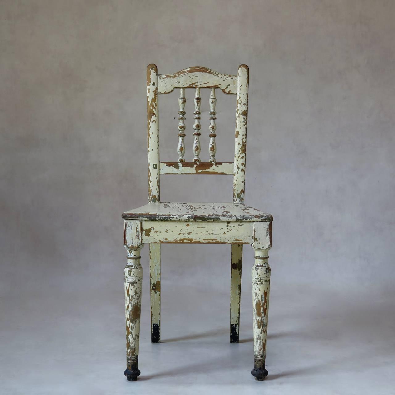 Set of three sturdy wooden chairs with petite backs and large trapezoidal seats. Original and heavily distressed cream-colored paint. The feet have been rather charmingly dipped in black.