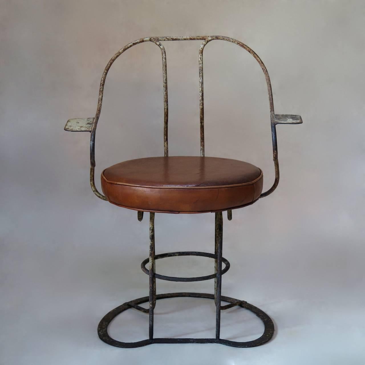 One-of-a-kind pair of wrought iron chairs with a lovely patina (traces of original white paint still very faintly visible). Great and unusual design. The round seats are covered in cognac-colored leather.