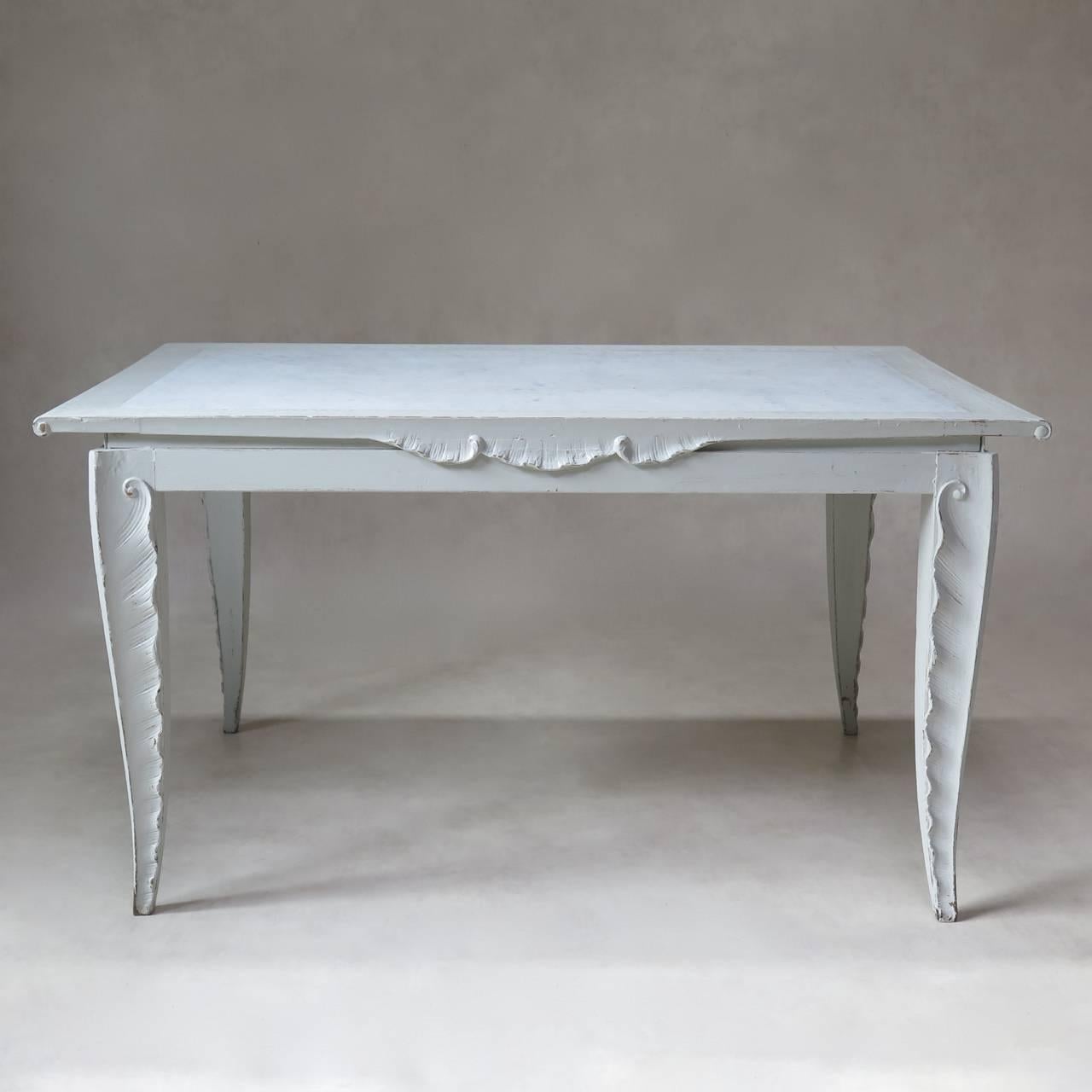 Elegant painted dining room table and four chairs of unusual design.

The rectangular table has a white marble top with a wood surround and is raised on tapering legs carved with a delicate scalloped palm-frond or feather-like design. The apron
