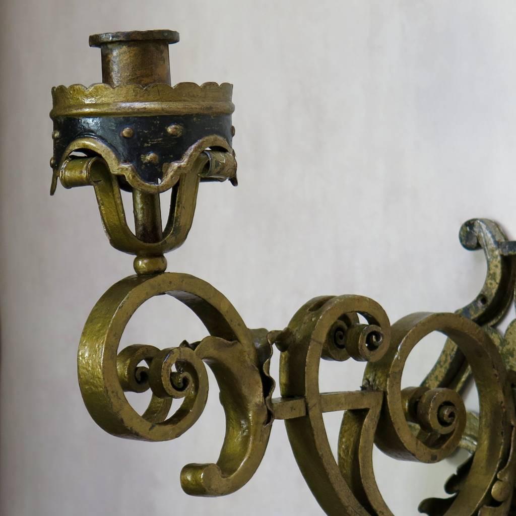 Set of seven heavy wrought iron sconces with elegantly scrolled bodies that fix onto a shield plate fixed to the wall. Adorned with acanthus leaf detail. Painted black and gold.