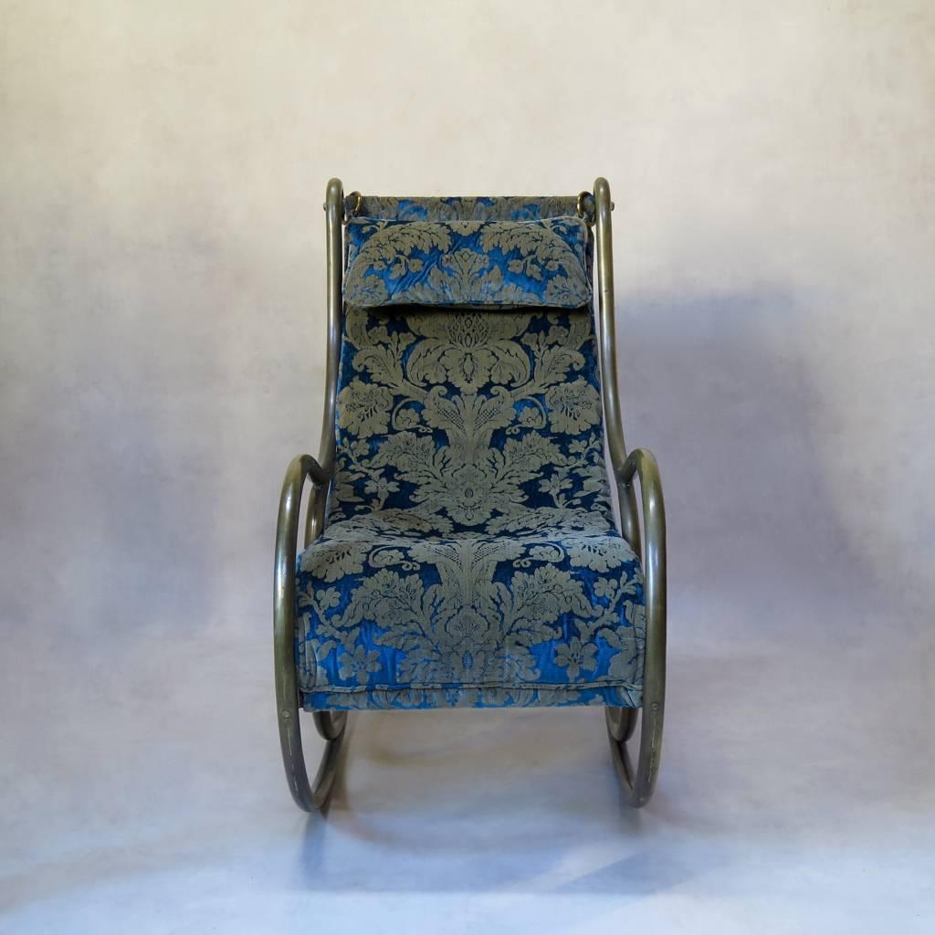 An unusual brass rocking chair with an agreeable, chunky frame that has acquired a nice patina over time. The seat is of padded peacock-blue velvet with a bold damask-style motif in gold.