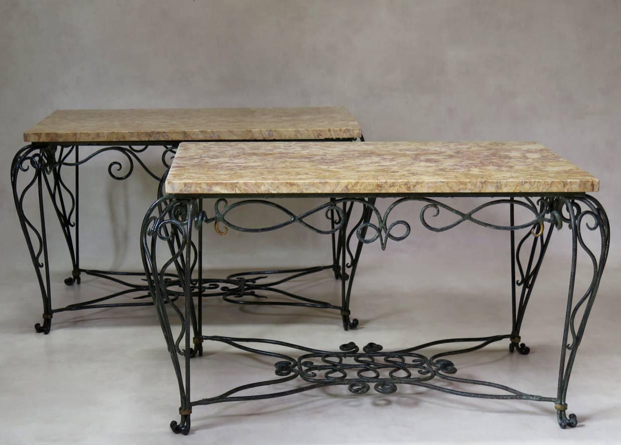 Very lovely, almost-pair of side or coffee tables. The wrought iron bases have elaborate curlicue motifs, and are painted dark green, with details picked out in gold. The design of the stretchers and aprons differ slightly. The tops are of yellow