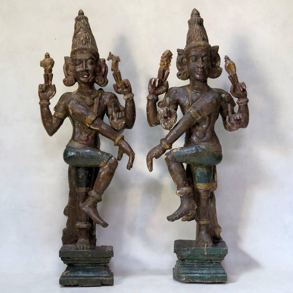 A pair of facing deities representing the Hindu god Vishnu. Made of exotic wood, coated with gesso and painted in soft brown, green and gold tones. The statues are raised on stepped pedestals. The backs are rough-hew and painted dark green, with a