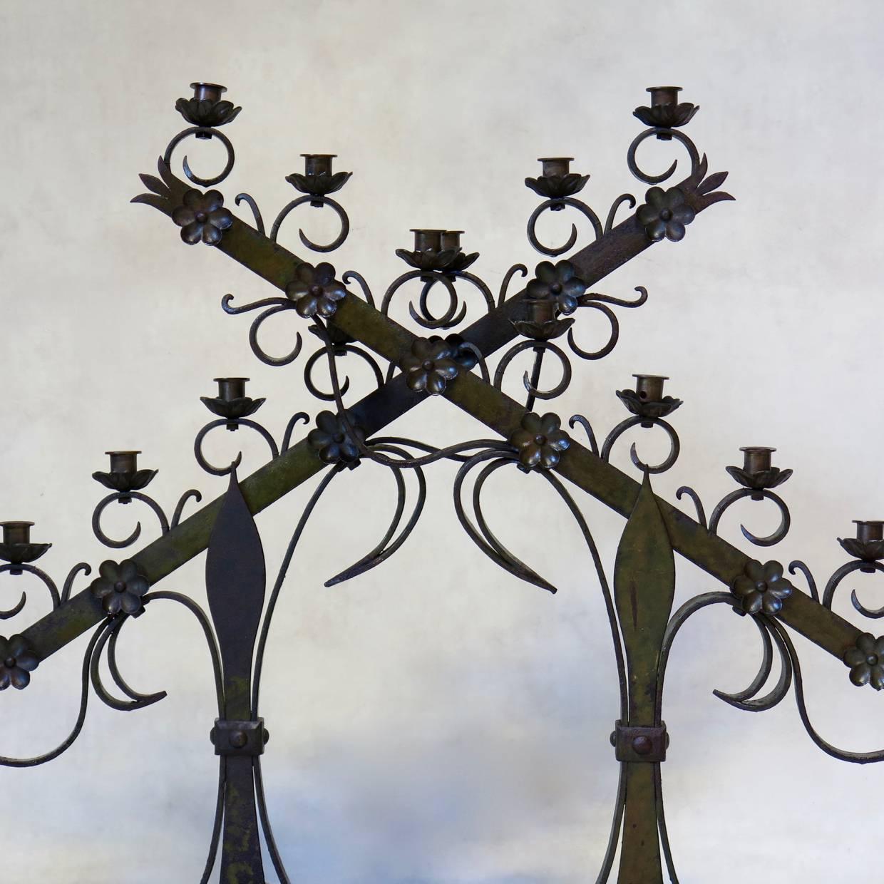 Fun and elegant pair of large iron candleholders, originally from a church. They are set on a losange-shaped wooden bases, with fleur-de-lys stem, and are decorated with rosettes and iron curlicues. 
These candleholders were wired once upon a time: