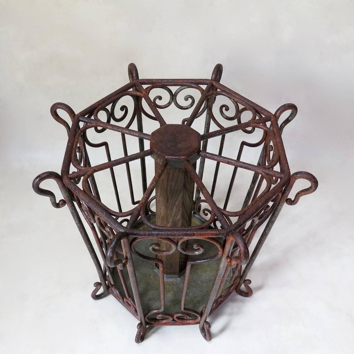 Rare and unusual large, circular umbrella stand made of heavy hand-wrought iron, with traces of original red paint. The stand has eight compartments arranged around a central oak shaft. Zinc-lined bottom.