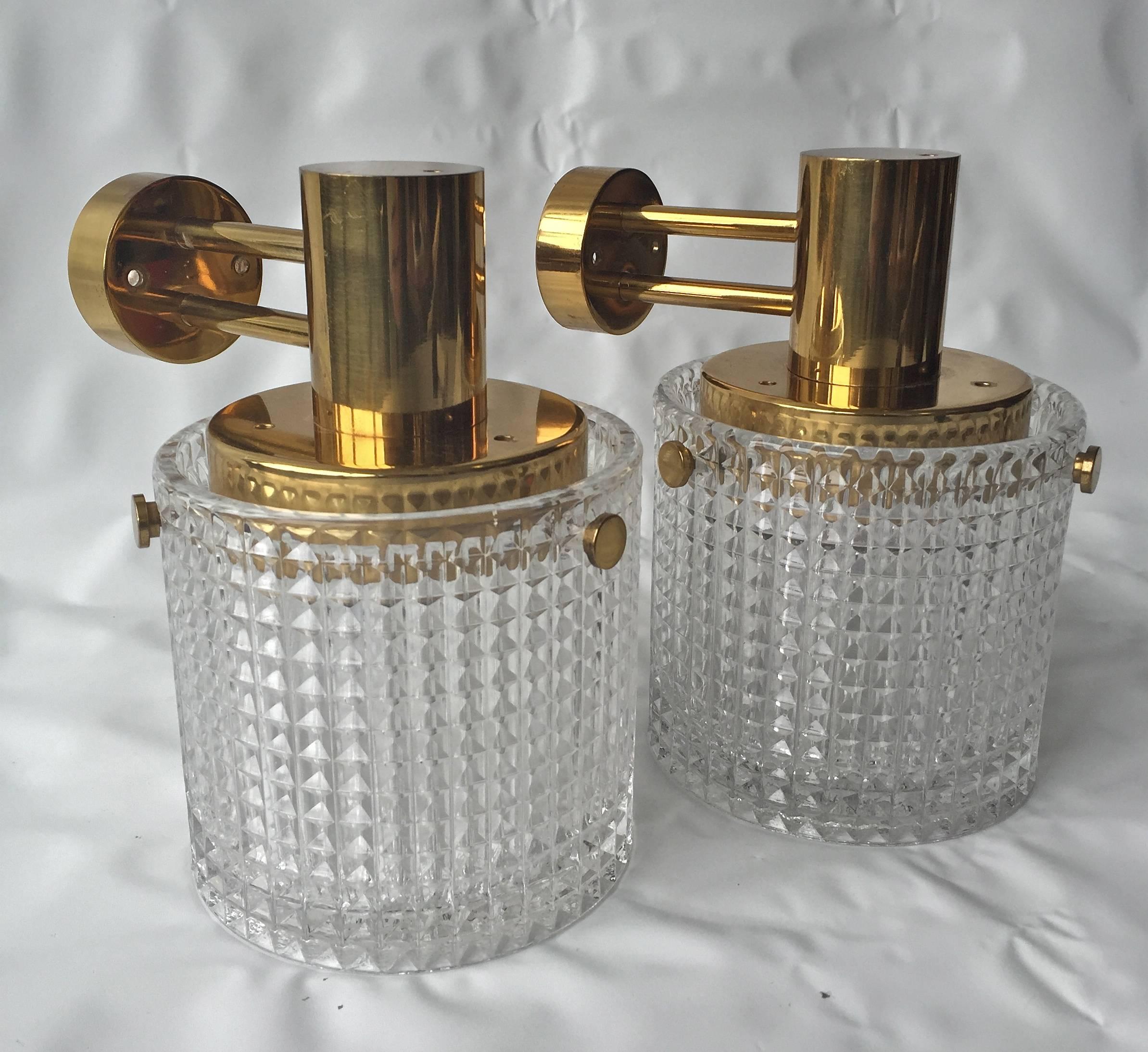 A pair of up or down head mounted wall lights, Orrefors attributed, Sweden, circa 1970s. Polished brass and textured glass. Measures: Diameter 5.5