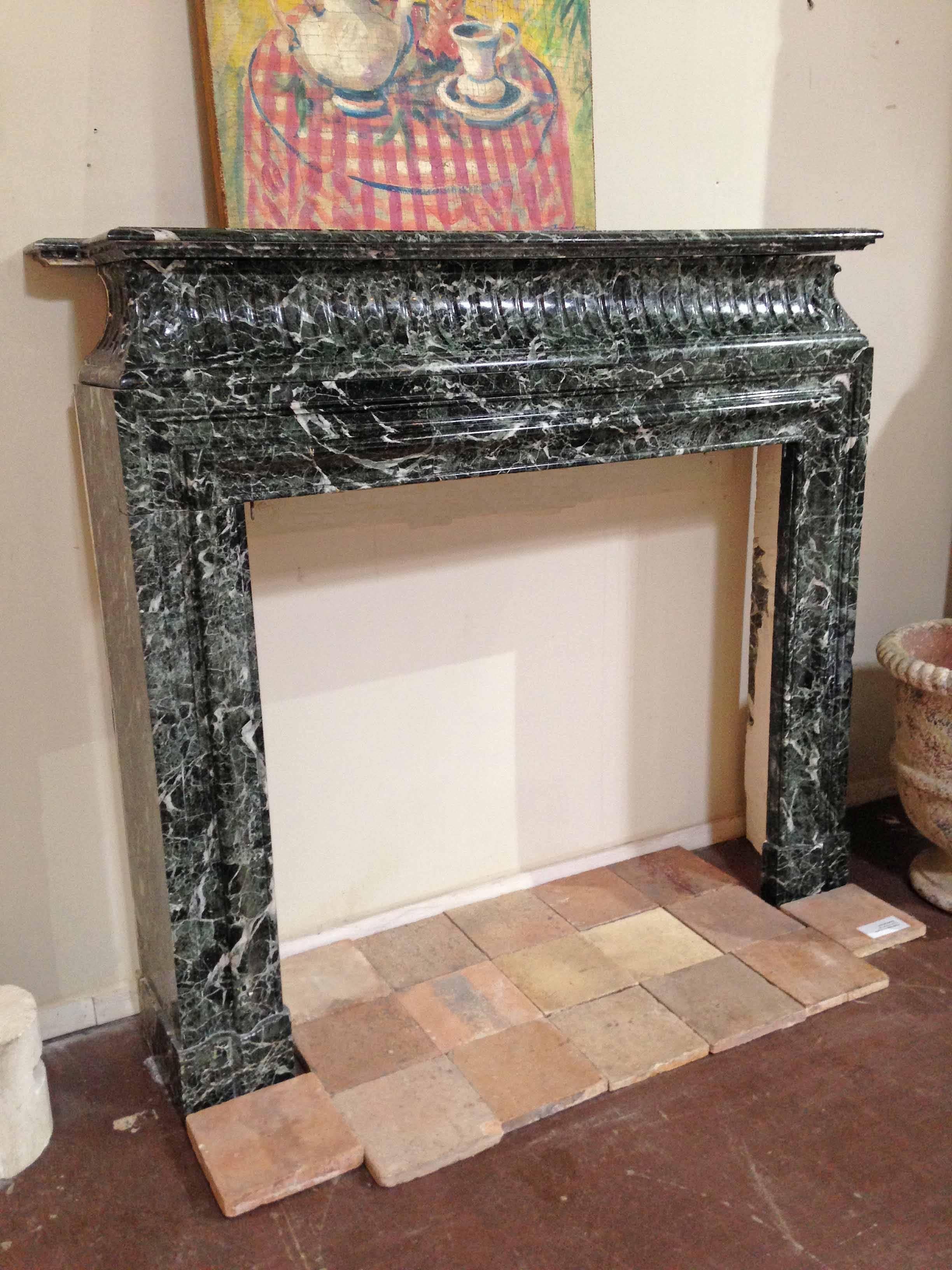 A sea-green Louis XIV style marble mantel with a deeply channeled lintel, topped with a double cornice for extra height. The straight lines of the carved moulding mirror the lines of the firebox, and are balanced by subtly carved acanthus leaves on