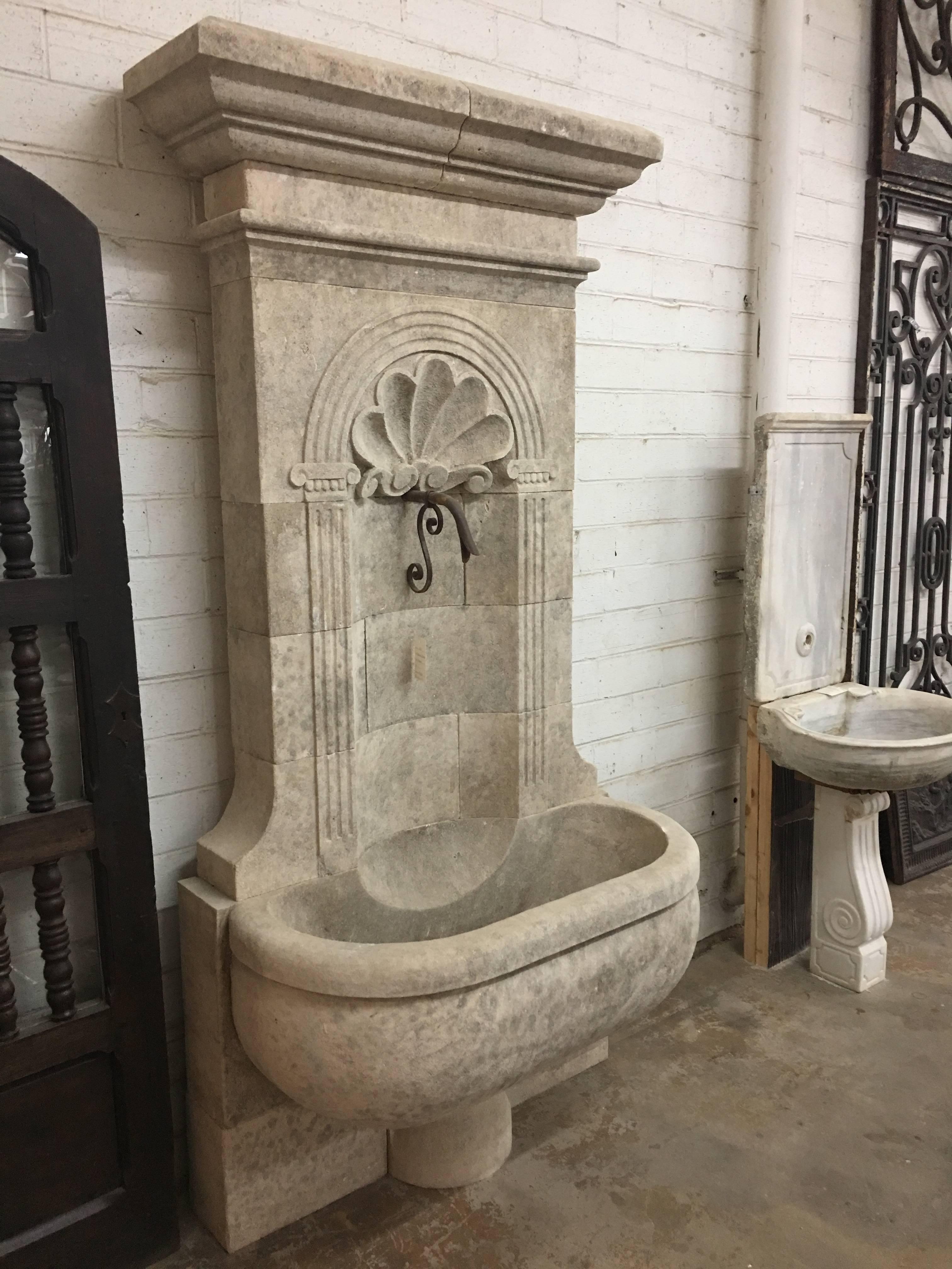 Here we offer a hand-carved limestone wall fountain of monumental proportions. The fluted columns and arch over the shell carving and water exit are all classic French design. The oversized bowl and overhanging crown are two more carved elements