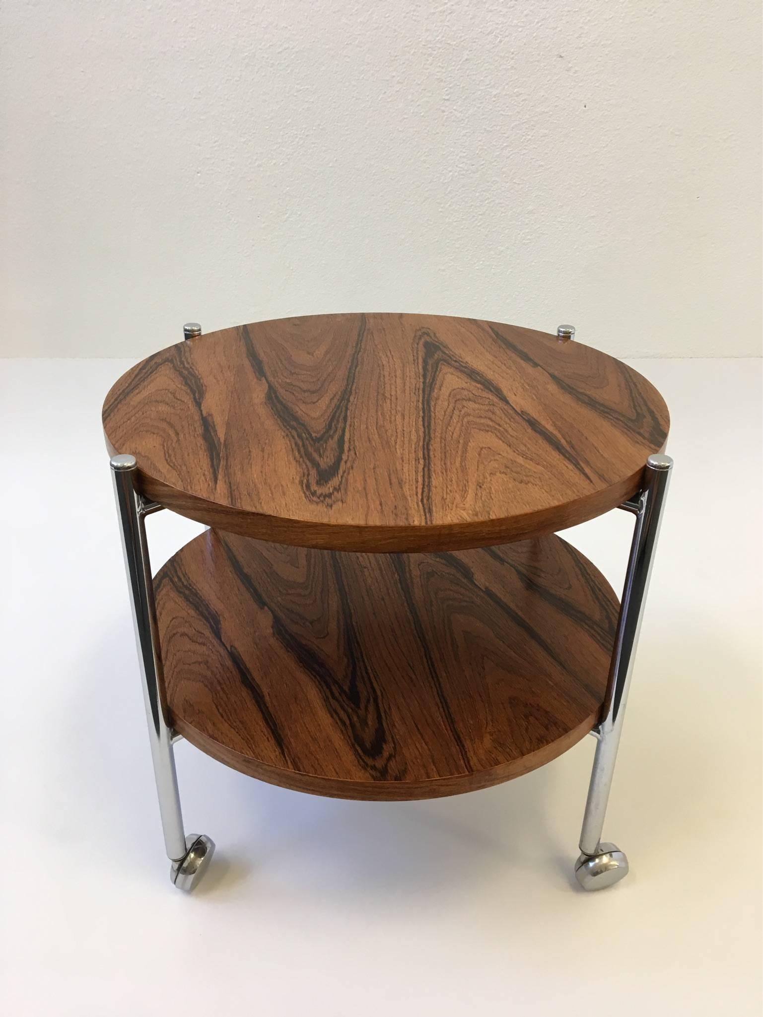 A beautiful two-tier rosewood and polished chrome side table on casters. The wood is press wood with a rosewood veneer. This is in original condition so it has some minor wear. 
Dim: 19