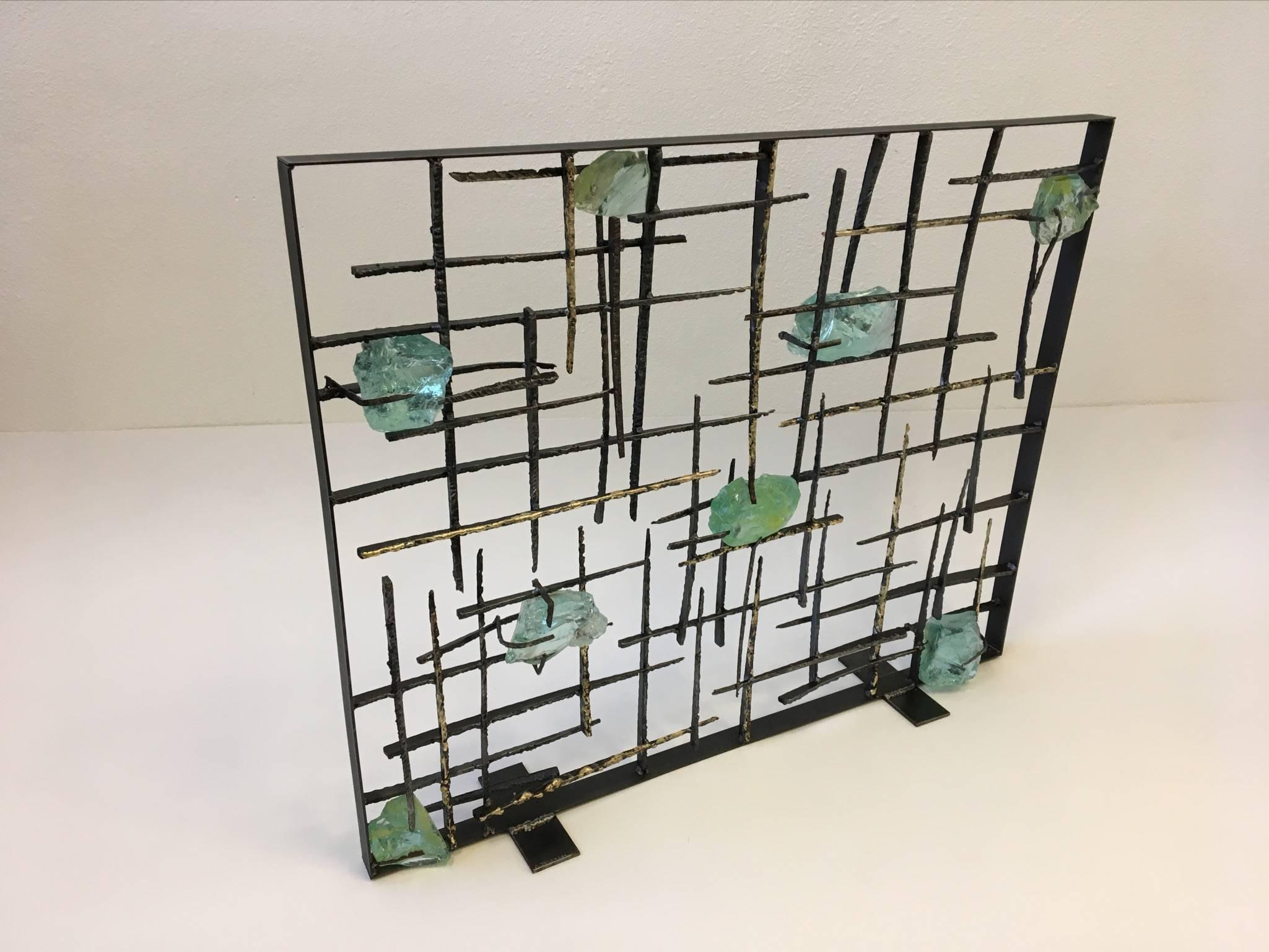 A beautiful Brutalist studio fireplace screen by American sculptor John De La Rosa. The screen is constructed of torch cut steel with randomly selected gilded edges with brass on some pieces and clear green with hints of yellow slag glass ( see