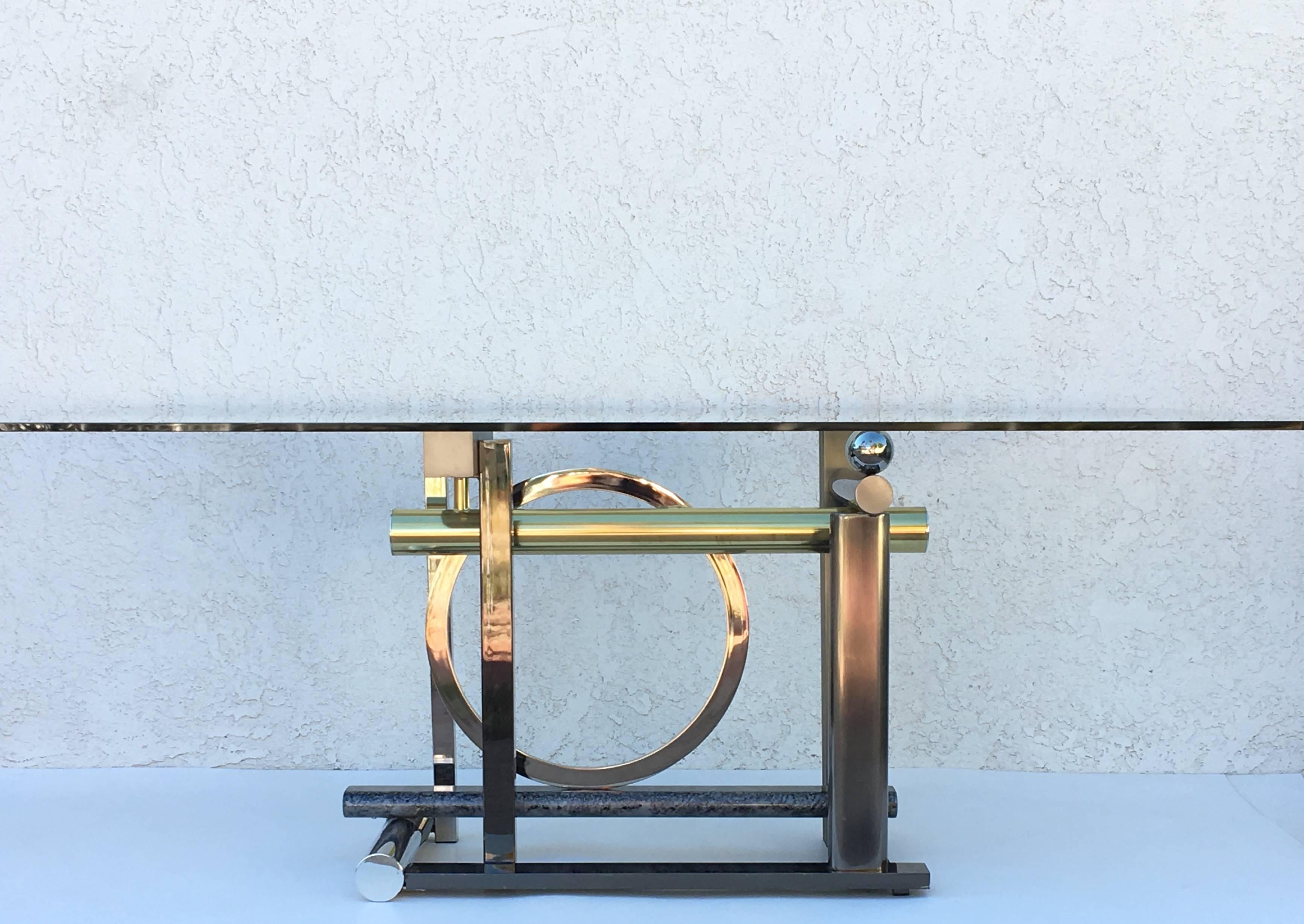 A sculptural postmodern dining table or desk design by Rick Lee for Design Institute of America in 1993

The base is made out of mix metals (brass, chrome, brushed stainless steel, gunmetal and many other finishes.
Measures: The glass top is 1/2