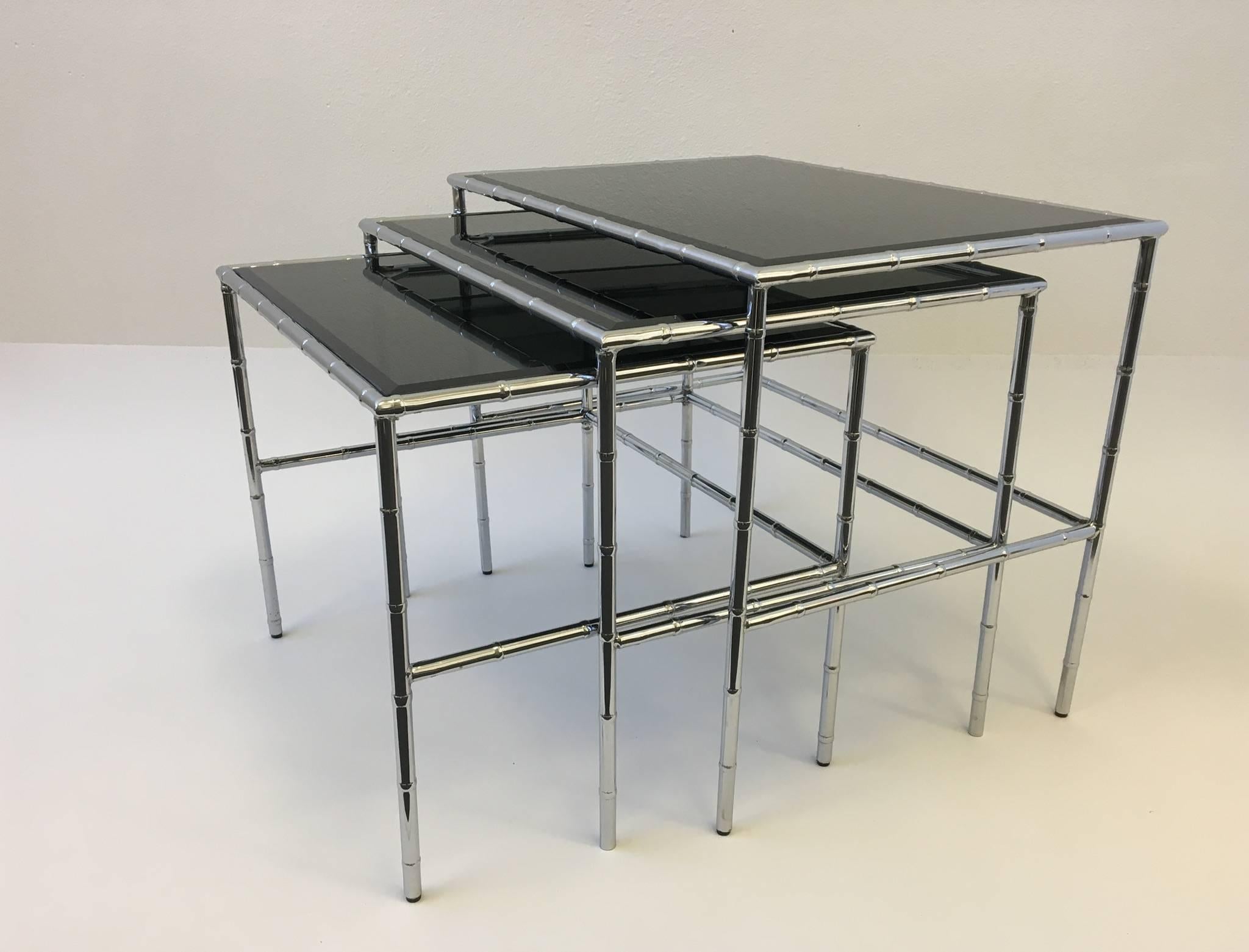 A set of three glamorous chrome and bevelled smoked glass nesting tables from the 1970s. The design of the frames are a faux bamboo with a polished chrome finish. The smoked bevelled glass top are new. 

Dimensions: Large: 20.25