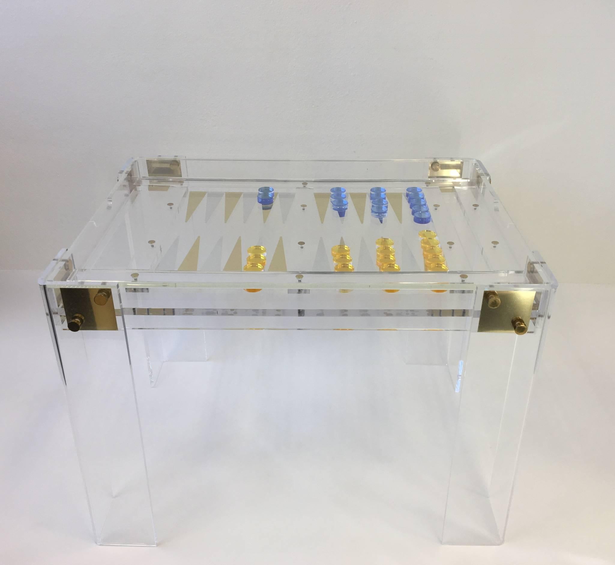 A glamorous clear acrylic with brass hardware designed by renowned designer Charles Hollis Jones in the 1970s. The table has a 1/2 inch thick acrylic top that goes over the backgammon board, so you can play cards also. 
The table has been newly