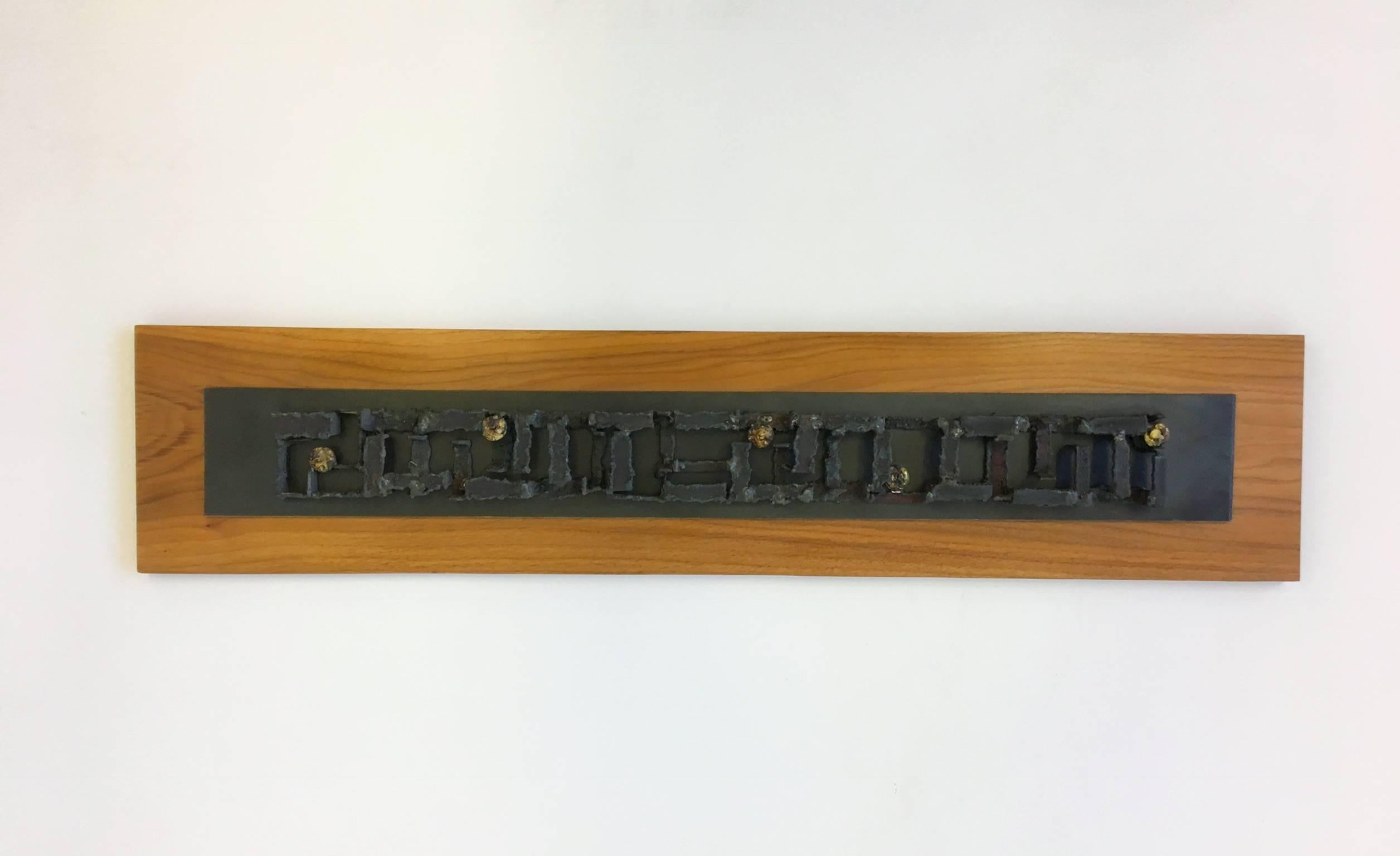 A studio Brutalist steel wall sculpture by John De La Rosa.
The sculpture is constructed with torch cut steel, with some bronze accents and mounted on a solid piece of walnut board. 
Dimensions: 40 inches high, 8.5 inches wide, 2 inches deep.