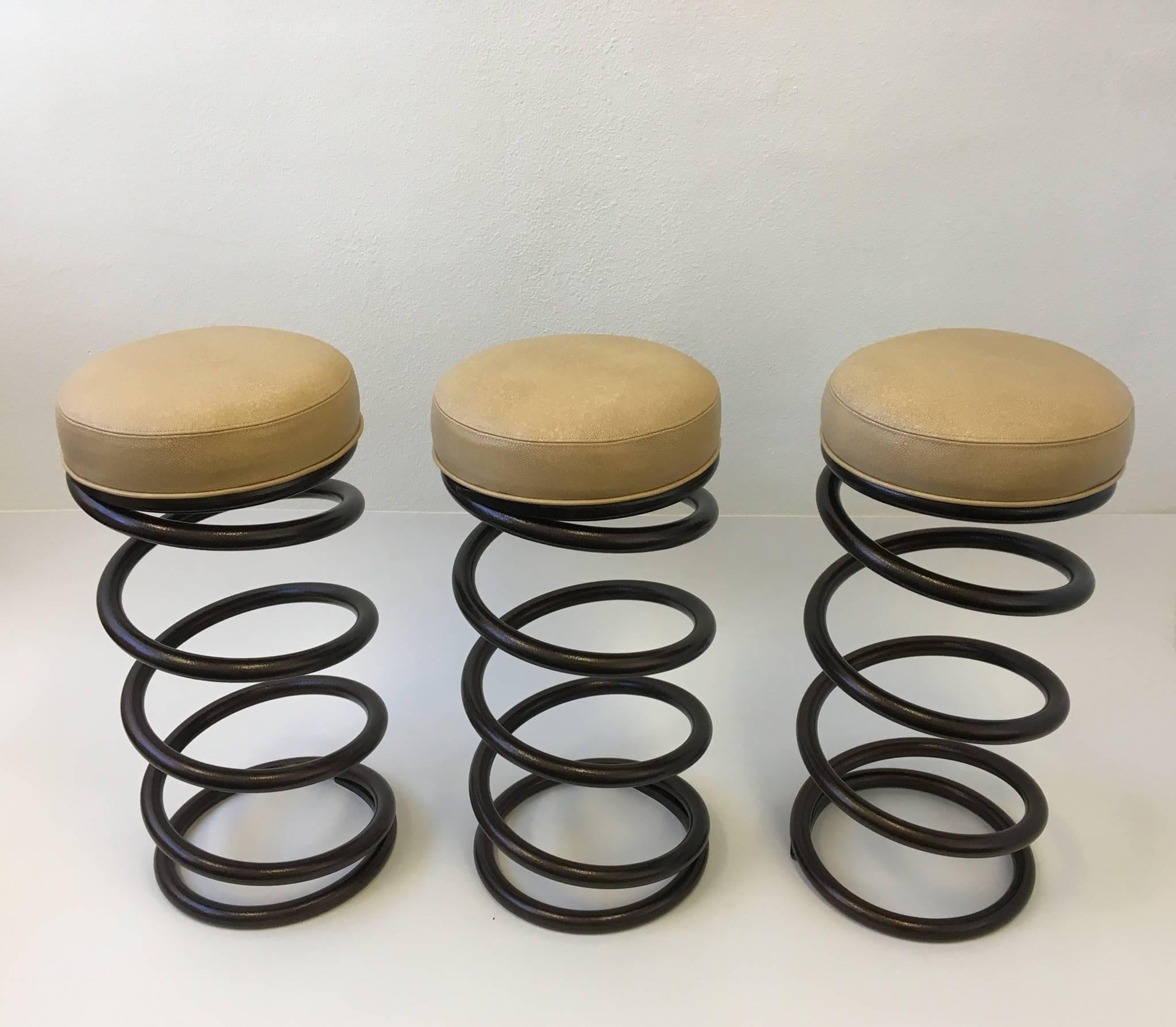 A set of three rare solid steel spring bar stools the seats have been newly recovered in cream leather embossed with a shagreen pattern. The bar stools have been newly restored. The spring has been powder coated with a brown copper tone orange peel