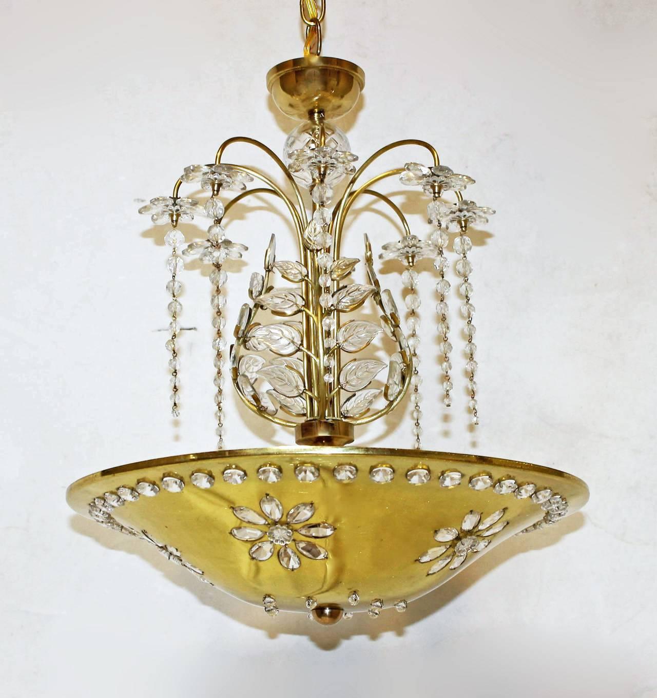 Beautiful dish form chandelier in the style of Maison Bagues. Polished brass dish is pierced with flower design and set with crystals that become illuminated with interior lighting. Center column is surrounded by crystal leaves and crystal flowers