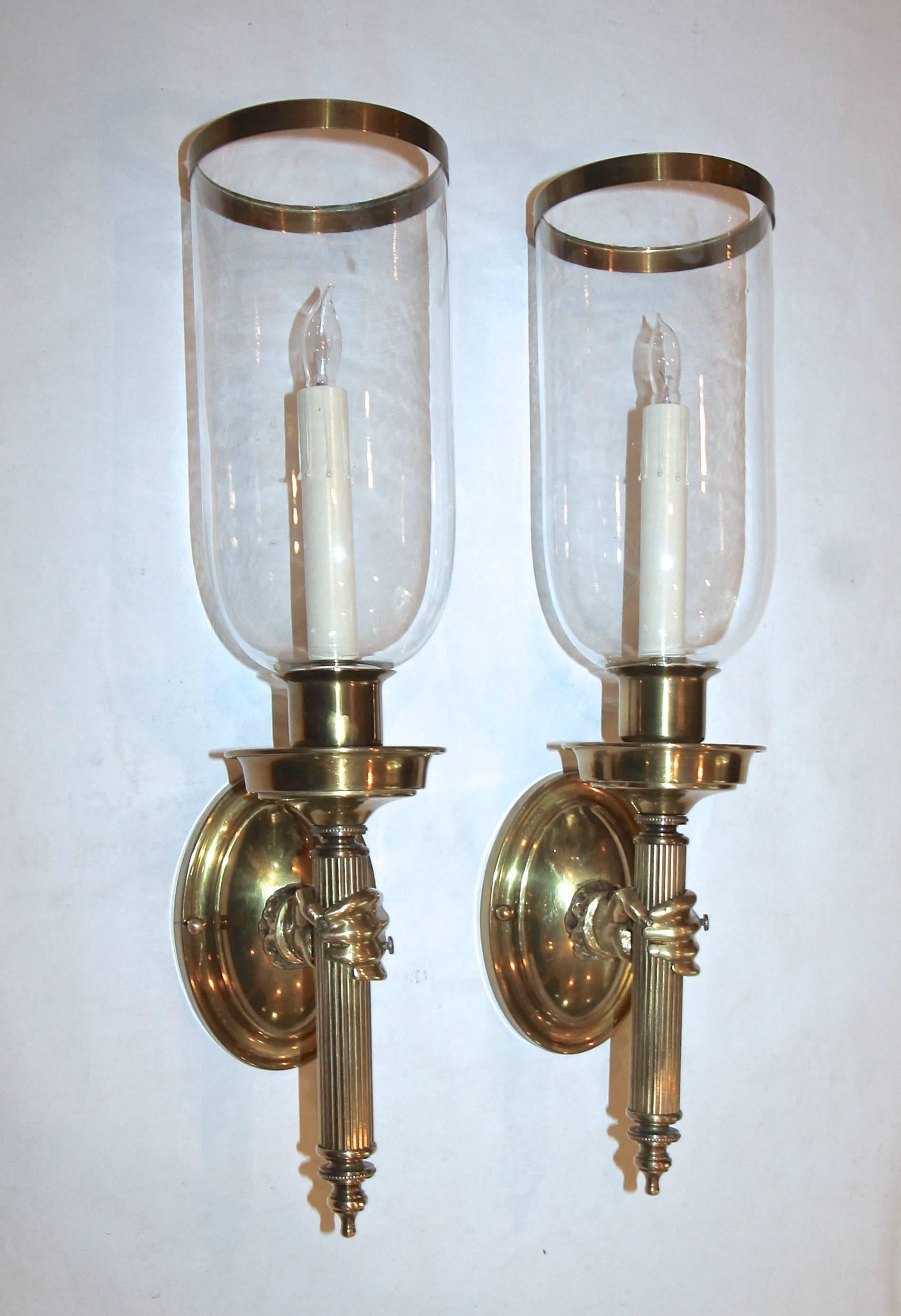 Pair of brass wall sconces of hands holding a torch. Large glass shades with brass outer rim included. Each sconce uses 1-40 watt max candelabra base bulb. Newly wired. Measure: Height without glass shade 16