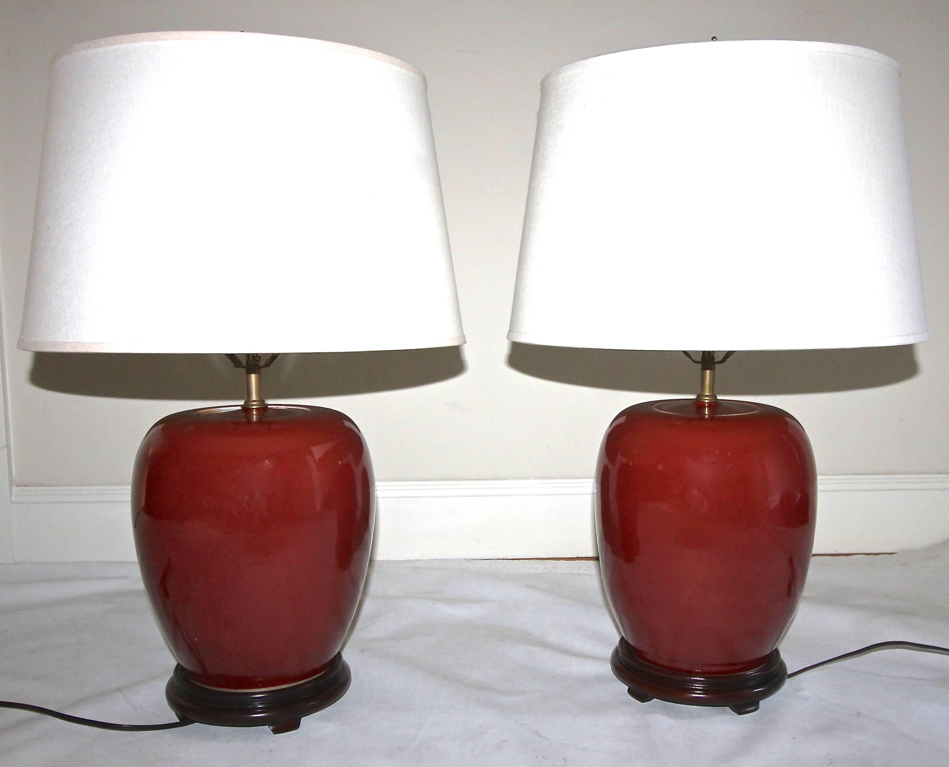 Pair of beautiful Chinese Oxblood porcelain vases mounted on wood lamp bases. Lamps include shades and finials. Height to socket (without shade) 18