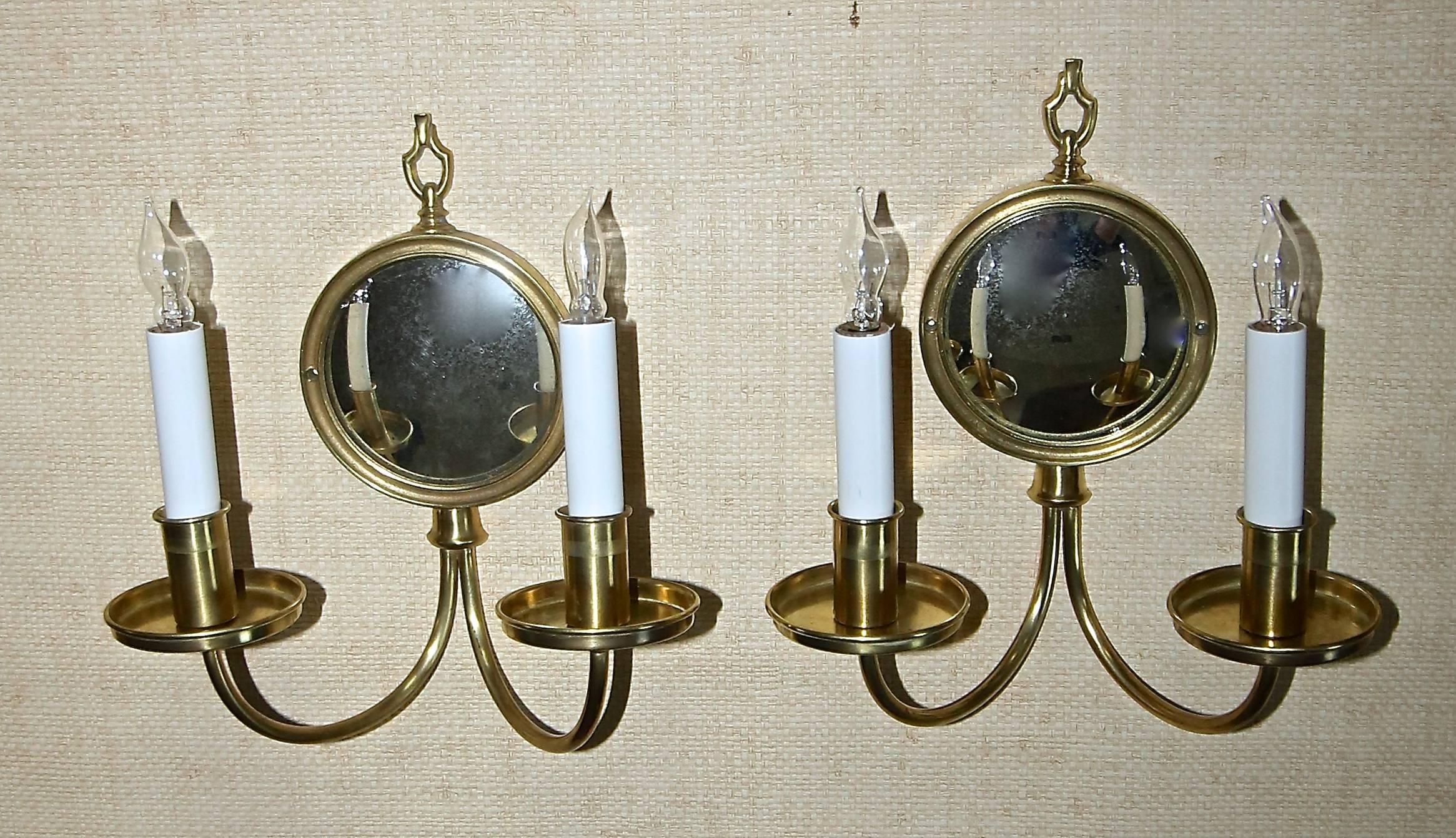 Pair 2 light brass wall sconces each with antiqued convex mirror backplate. Each sconce uses 2-40 watt candelabra base bulbs. Round brass backplates are 4 7/8" diameter. Newly wired.