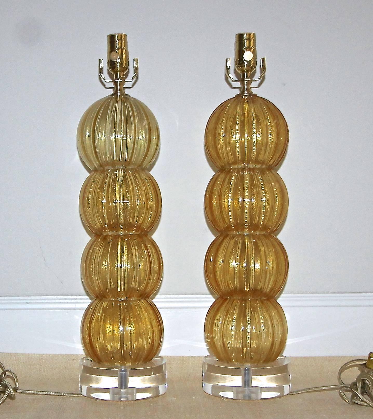 Pair of Italian blown glass Murano lamps in amber with gold inclusions. Each lamp has four stacked ribbed ball shape globes mounted on custom acrylic bases. Newly wired for US with French style rayon covered cords and new brass fittings.

Measure: