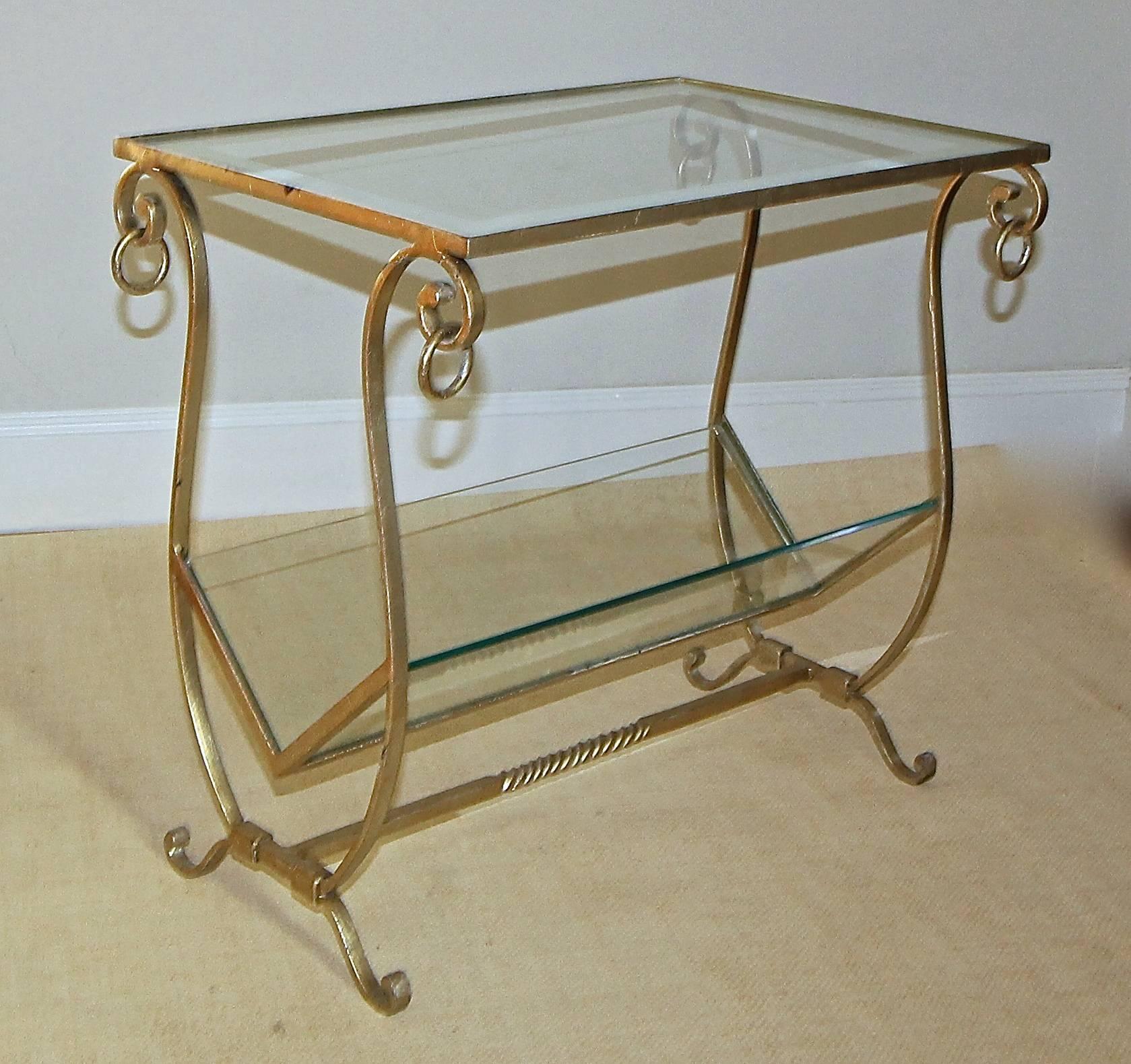A fine gilt iron side table with lower shelf magazine self. Inset glass top has a mirrored edge. Lower magazine shelf with clear glass.
