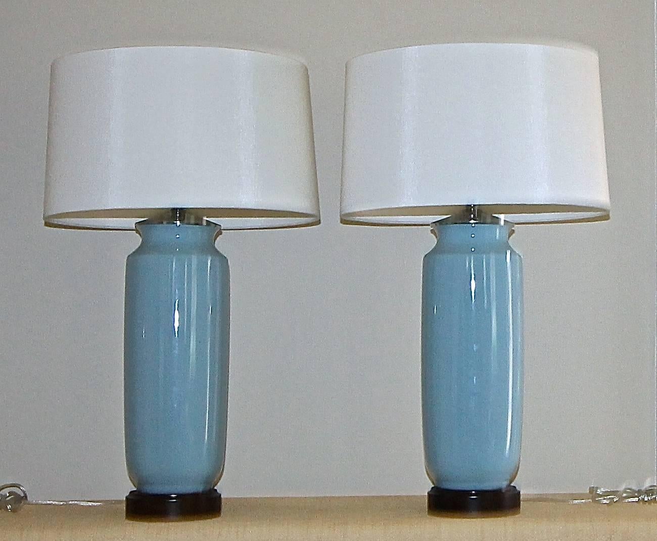 Pair of high end custom pale blue ceramic lamps on turned wood bases in dark brown finish. Nickel finish fittings and newly wired with full range dimmer sockets. White fabric shades are included. Overall height including shades 28", height