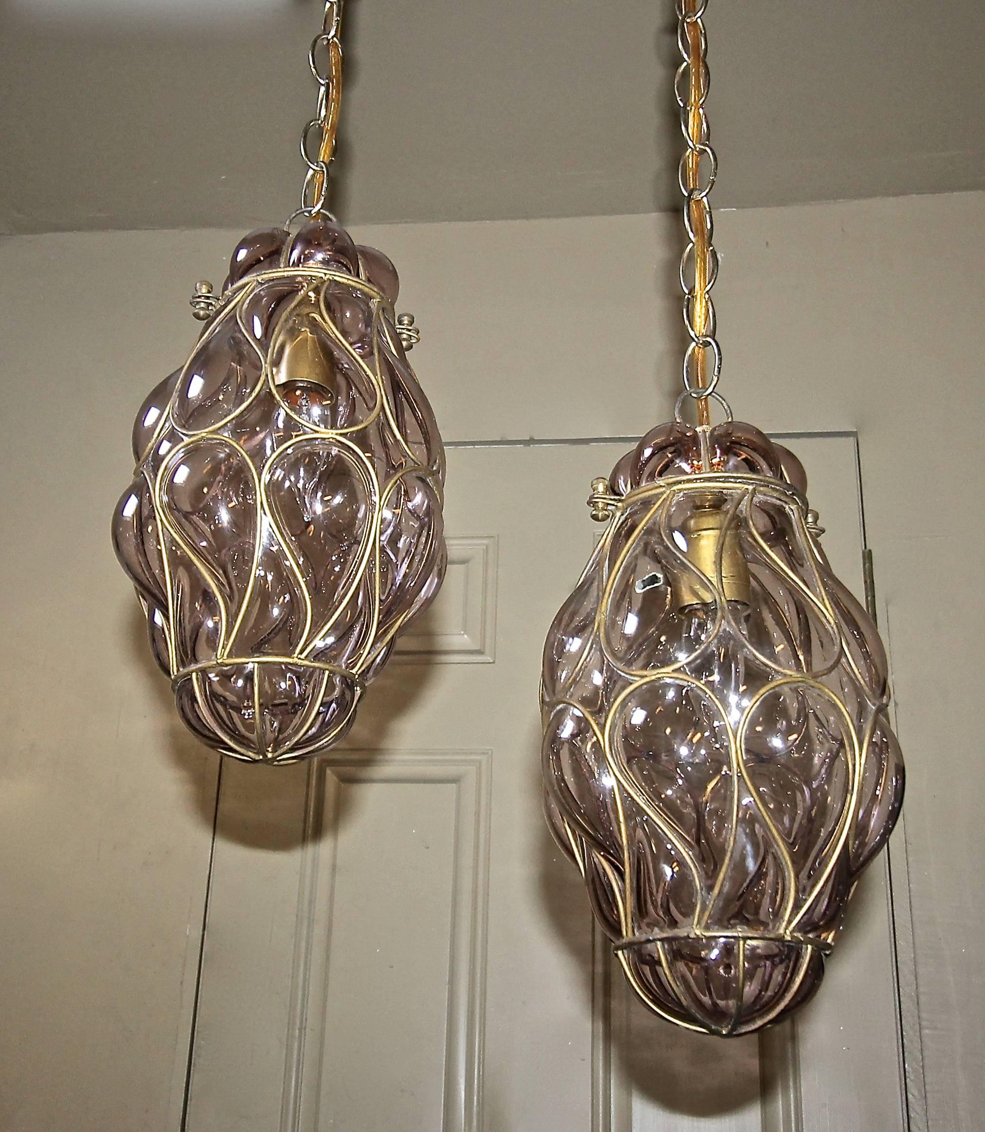 Pair of Italian Venetian wire cage amethyst color (pale purple) glass and brass finish metal pendant or lantern lights. Each fixture uses one 60-watt "A" base bulb Newly wired. Size of each fixture 13" tall x 7" wide, overall