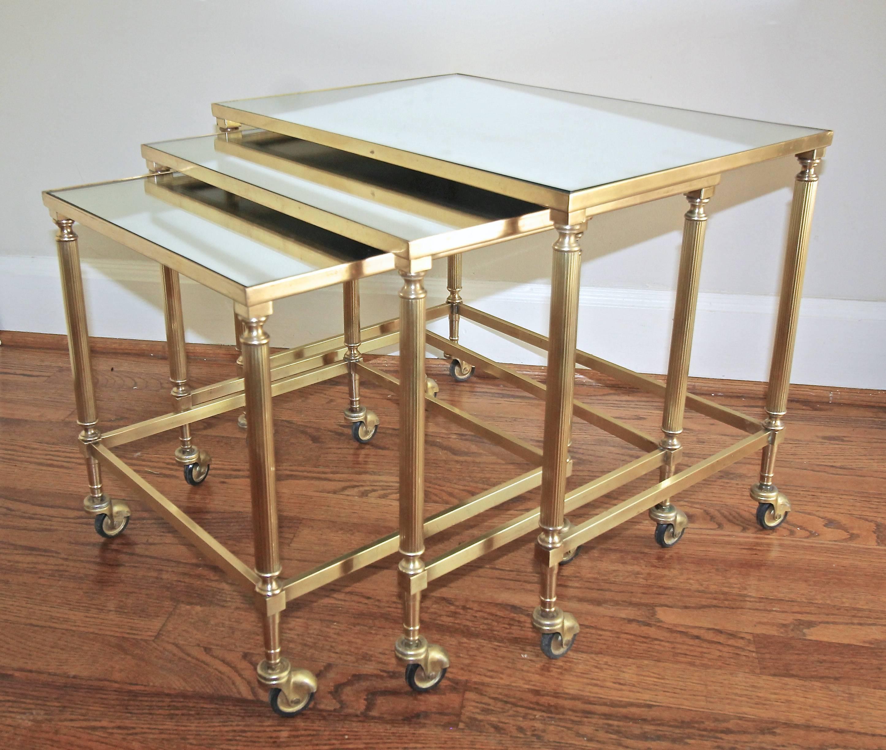 A lovely set of three French brass nesting tables with inset mirrored top. Reeded brass legs are set upon capped casters. 
Size each table:
1) 20.5