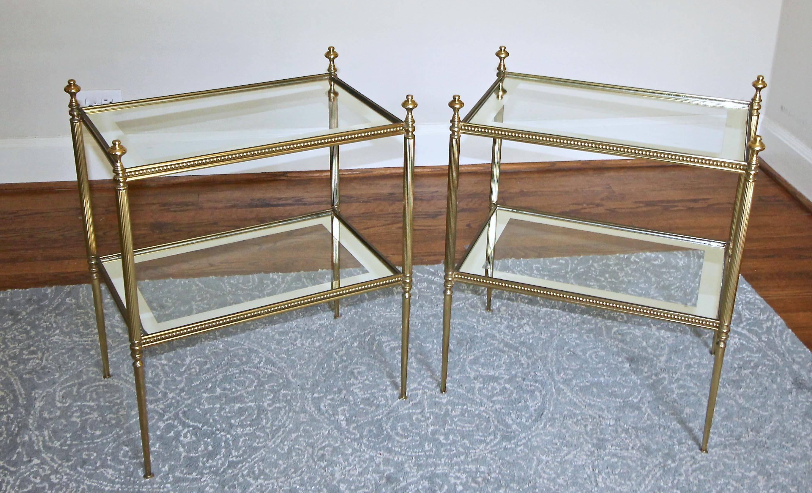 Pair of (two) French two-tier side or end tables with inset glass tops with mirrored edges in the manner of Jansen. Solid brass fittings are nicely detailed with a beautiful applied beaded detail to horizontal elements. Tables retain original finish