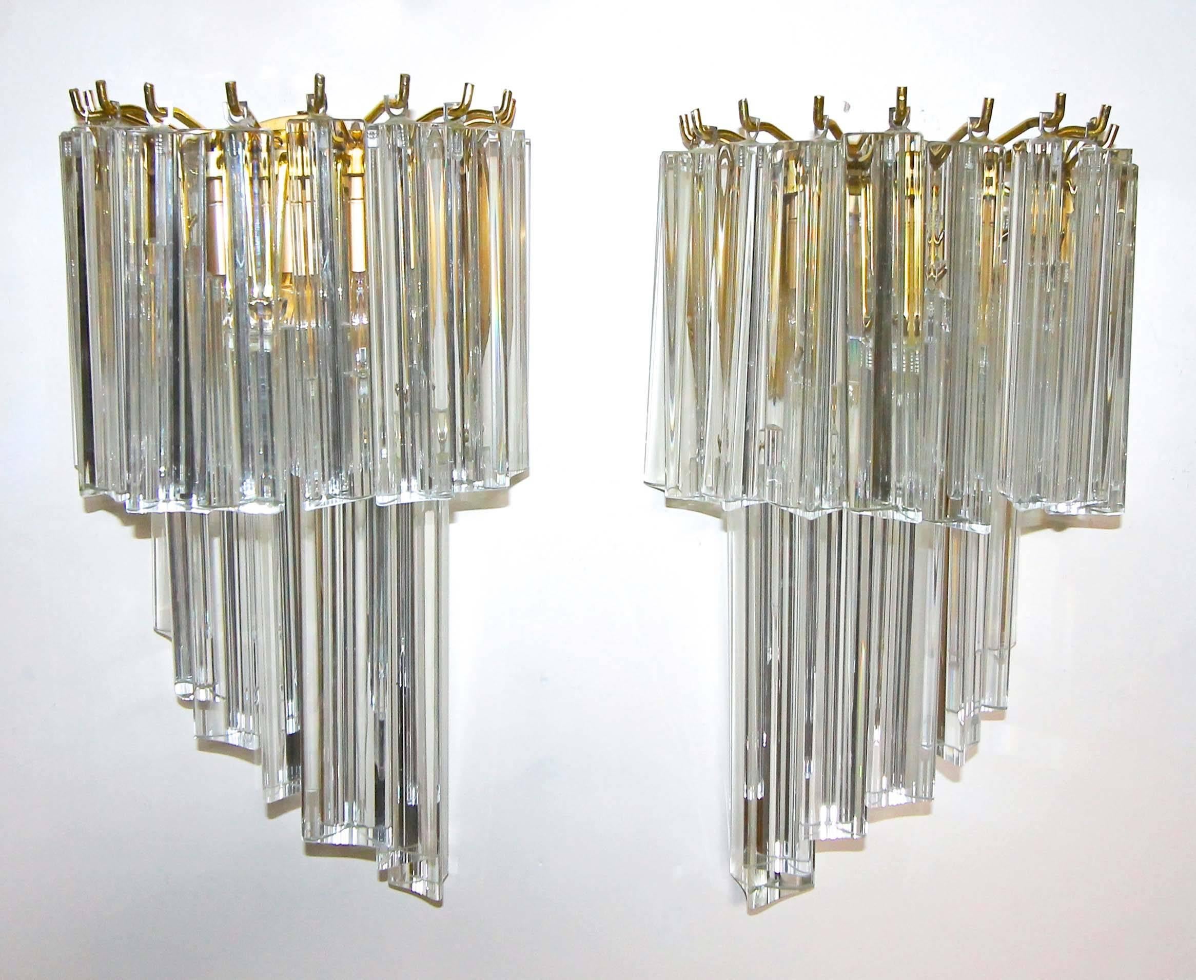 Pair of clear crystal glass triedi or triedri prism wall sconces in a cascading shape in the style of Venini. Solid brass backplates in a warm brushed finish with similarly finished fittings. Each sconce uses one candelabra 