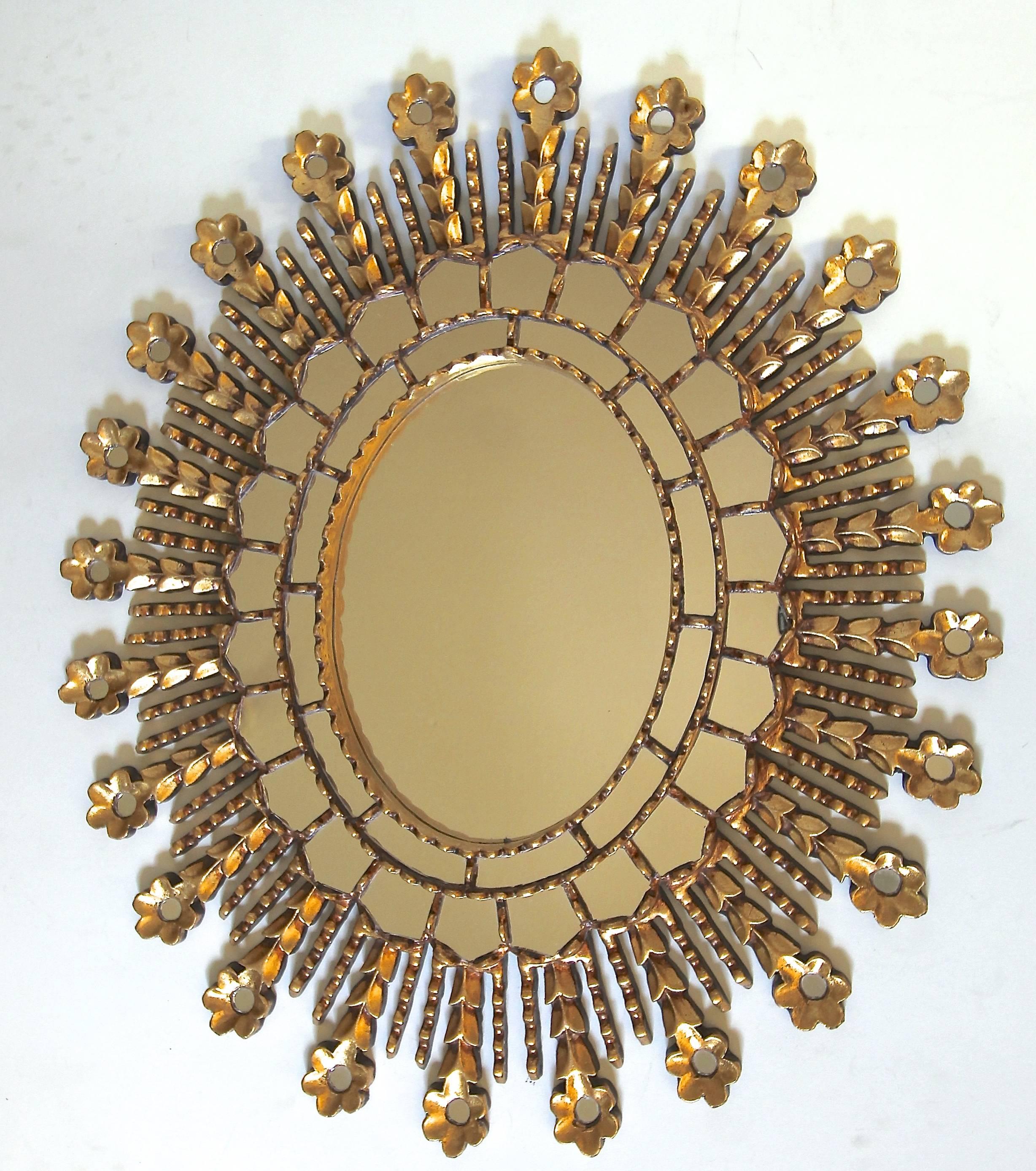 Hand-carved giltwood sunburst oval shaped wall mirror. Two rows of small inset mirrors encircle the large central mirror with carved gilt details. An additional row of inset circular mirrors in flowers surround outer details of mirror.