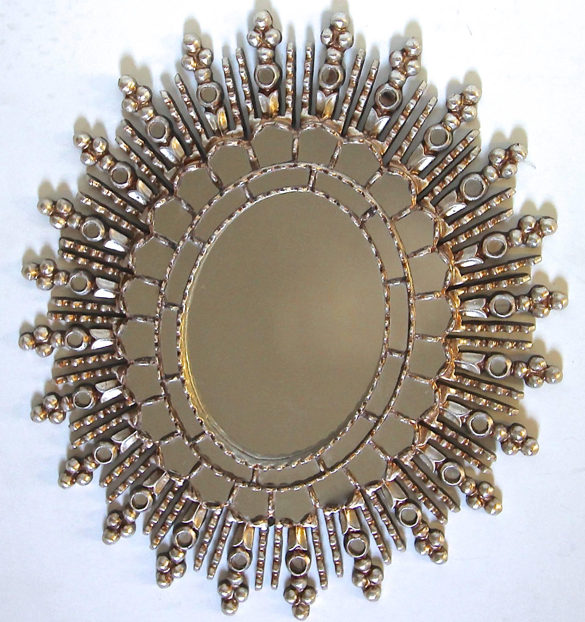 Hand-carved oval shaped silver colonial Spanish style wall mirror in a silver gilt finish. Two rows of small inset mirrors encircle the large central mirror with carved silver gilt details. An additional row of inset circular mirror surrounds outer