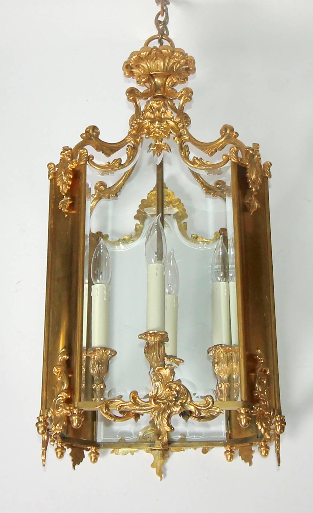 A heavy and well-crafted French doré gilt bronze lantern in the Louis XV or Rococo style. Octagonal form with four inset glass panels alternating with four smaller gilt bronze inserts and acorn finials at base. Glass panels are beveled to follow the