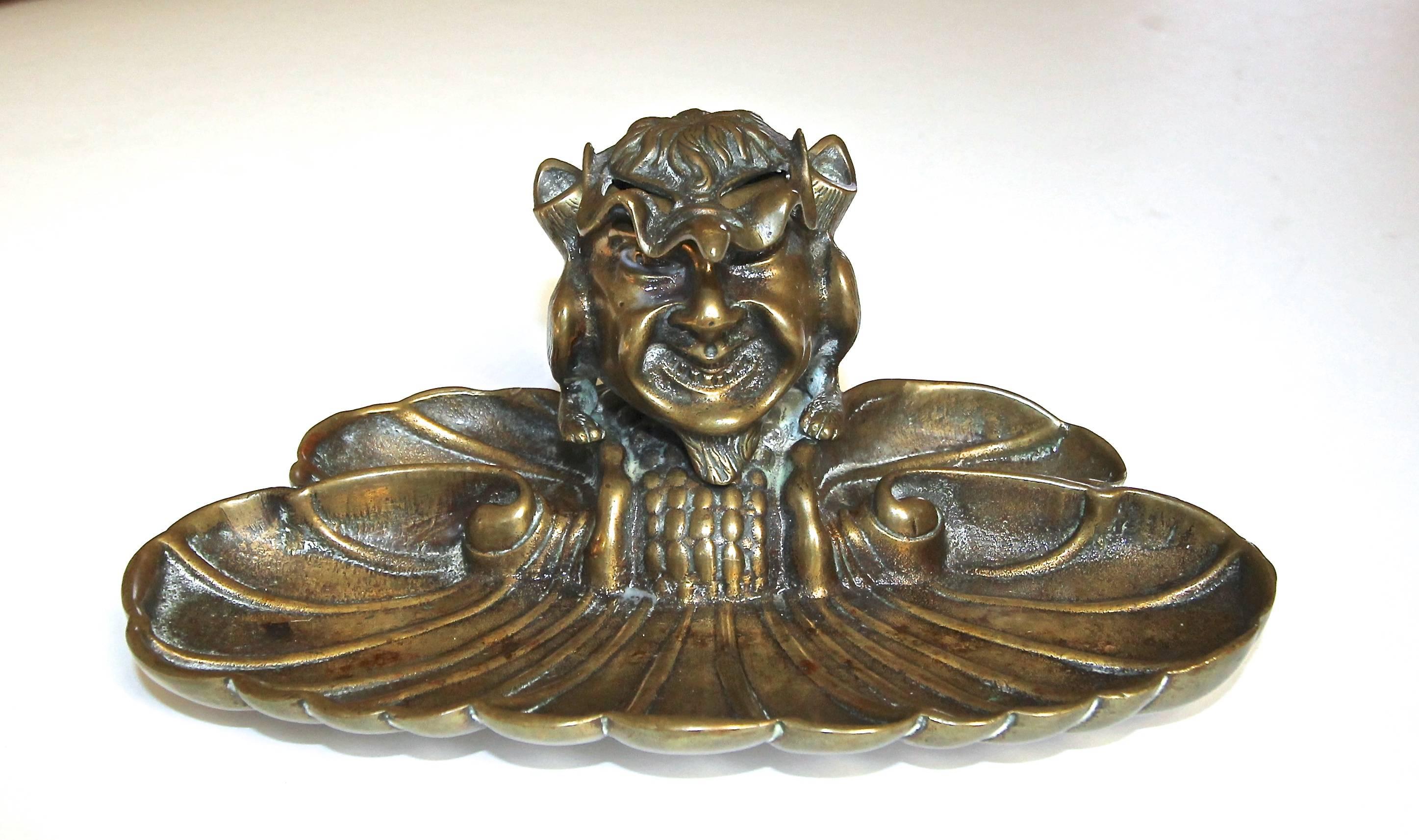 A whimsical bronze or brass late 19th or early 20th century inkwell with a grotesque style footed gargoyle mounted on a shell form base.