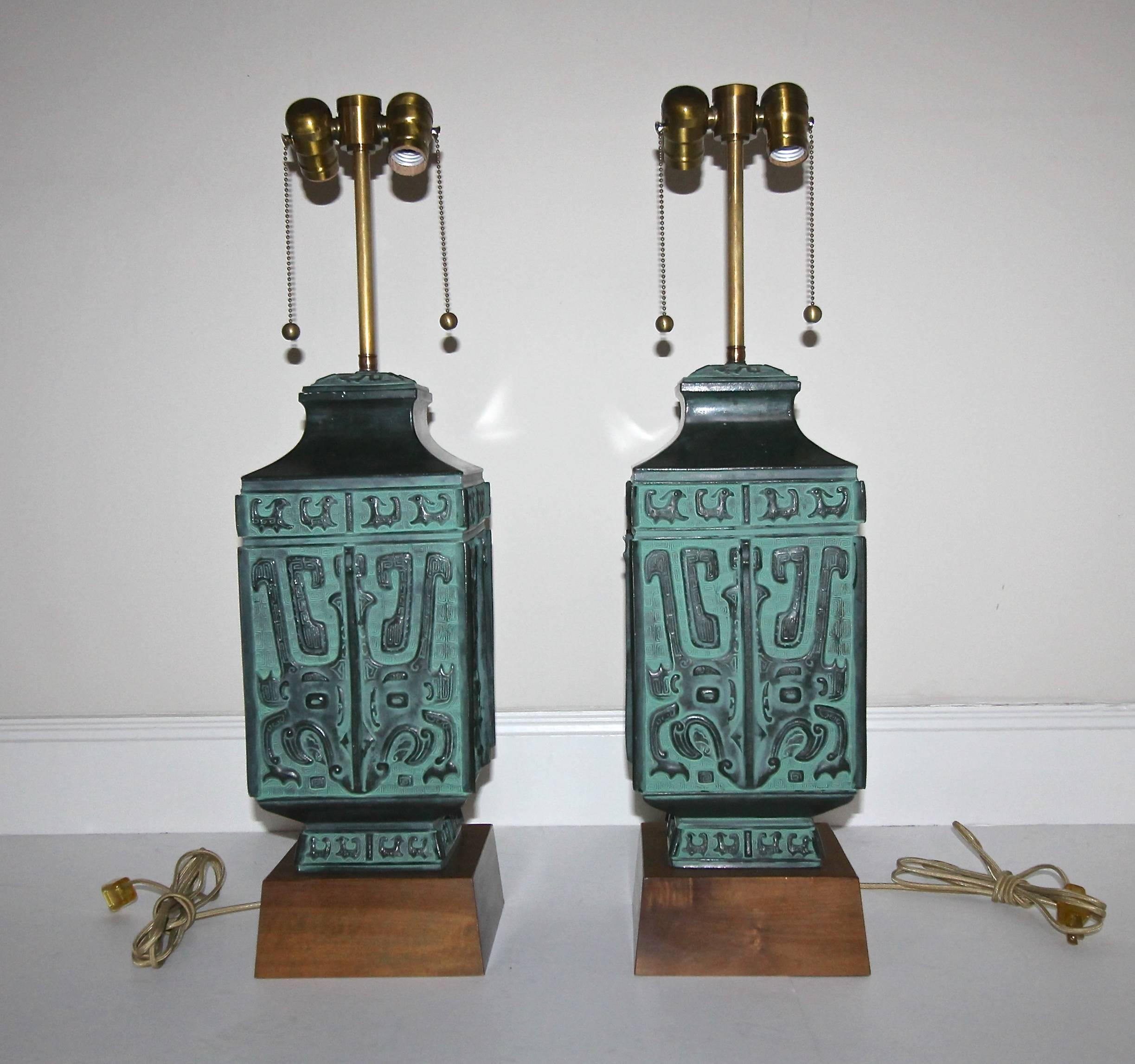 Pair of large cast metal table lamps in the manner of James Mont featuring archaic Chinese designs with a patinated verdigris finish on custom wood bases. Newly wired for US with double cluster brass sockets and rayon covered cords. Shades are not