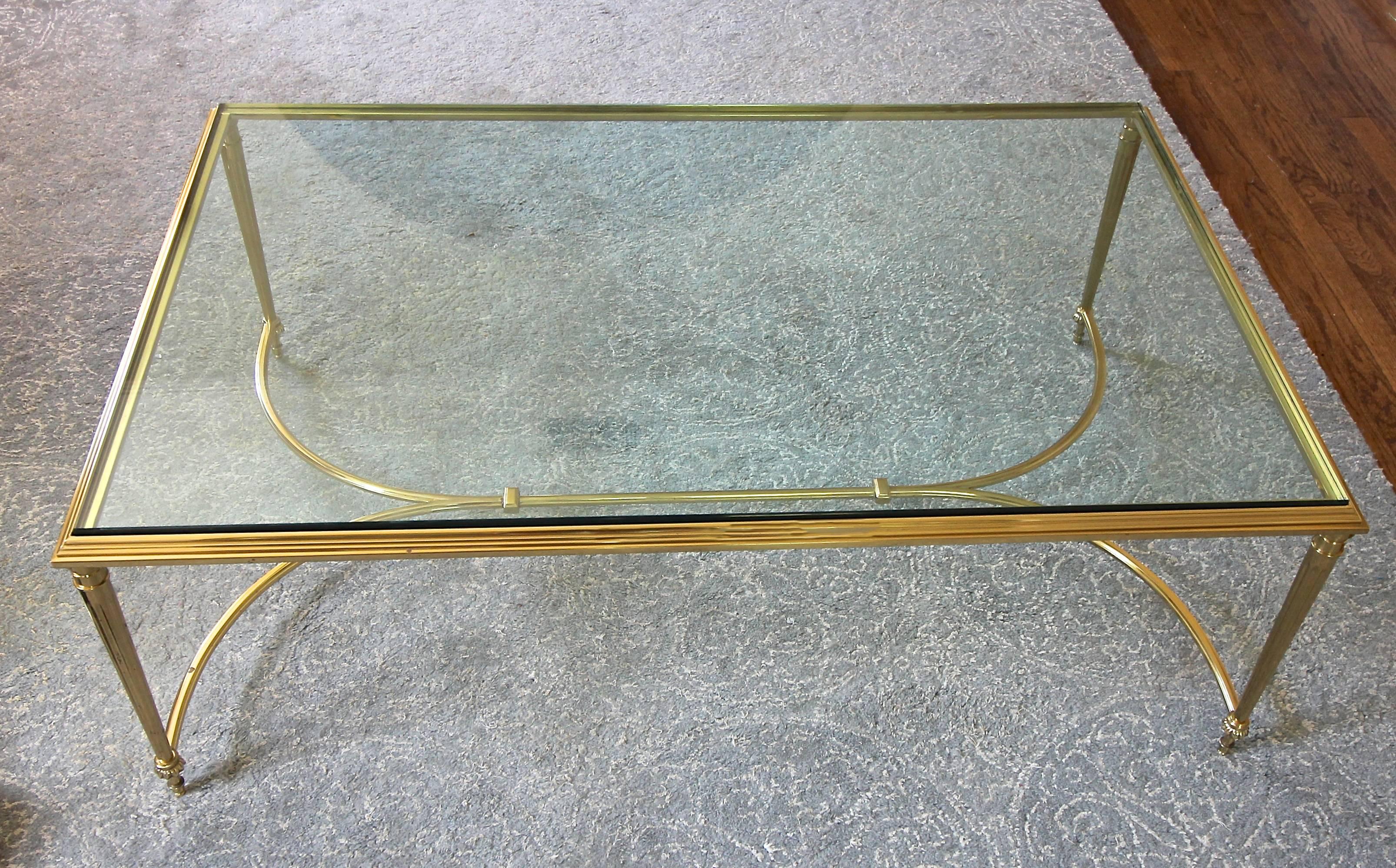 Large-scale cocktail or coffee table beautifully crafted from solid brass in the French Louis XVI style with fluted column legs, detailed stretcher and decorative escutcheons at base. Thick and heavy clear inset glass top. Table is extremely well
