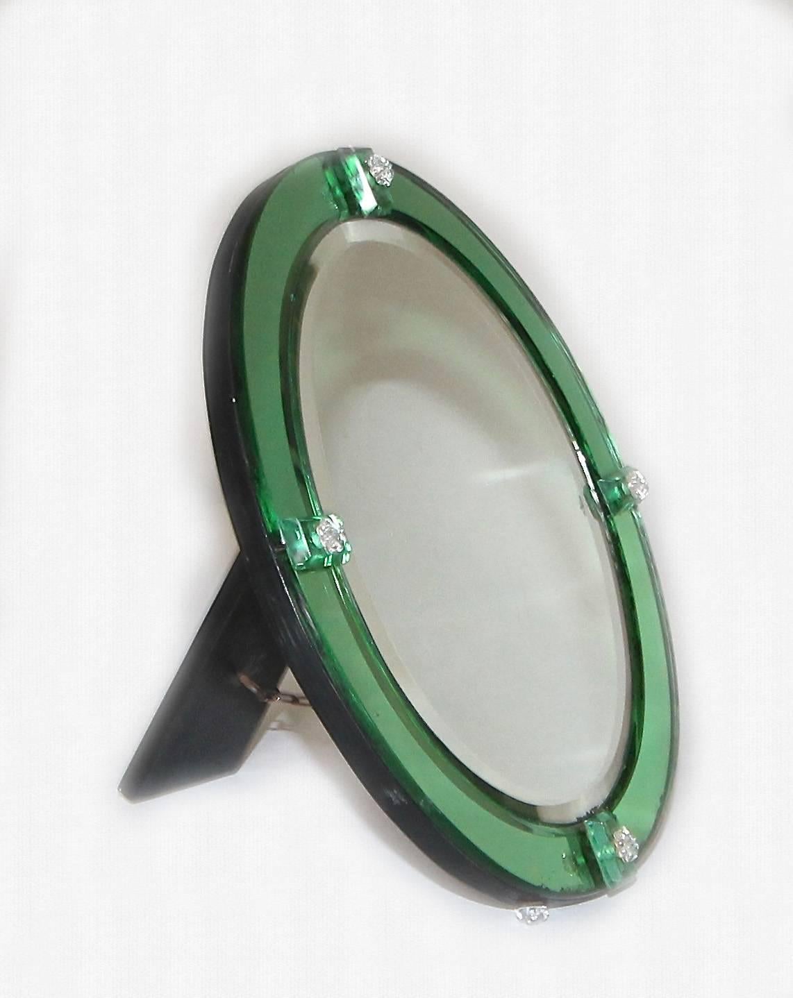 Rare diminutive oval mirror bordered with emerald green mirrored glass panels. Glass panels are held in place with decorative blown glass pins. Black painted wood backing and easel Stand held with brass chain.