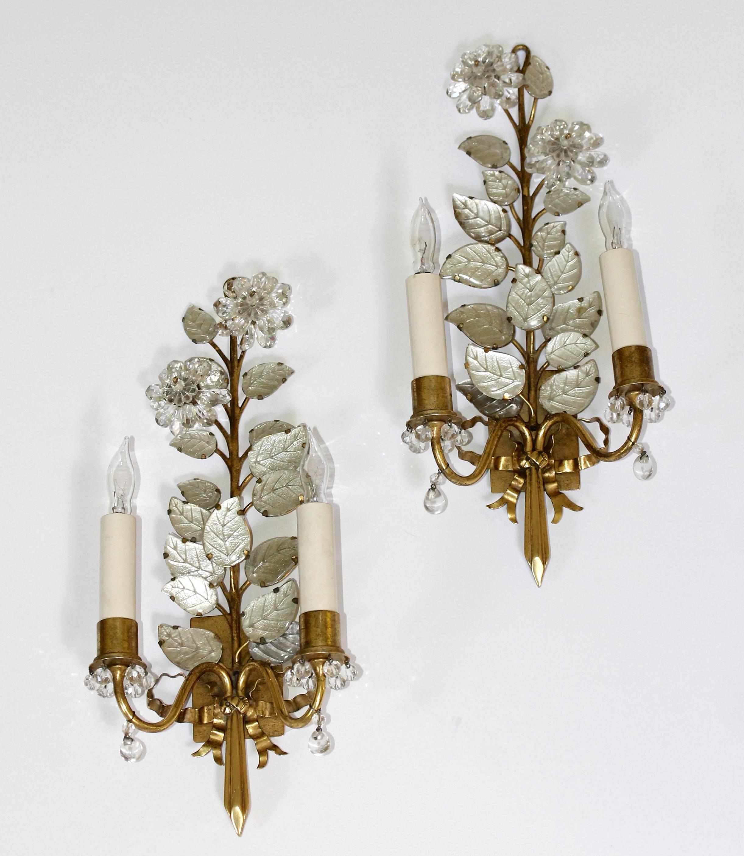 An exquisite pair of gilt bronze two-light floral wall sconces decorated with delicate crystal flowers and glass leaves. The lights are further enhanced by stems tied with a decorated ribbon motif. Sconces are in mirror image. Each uses two