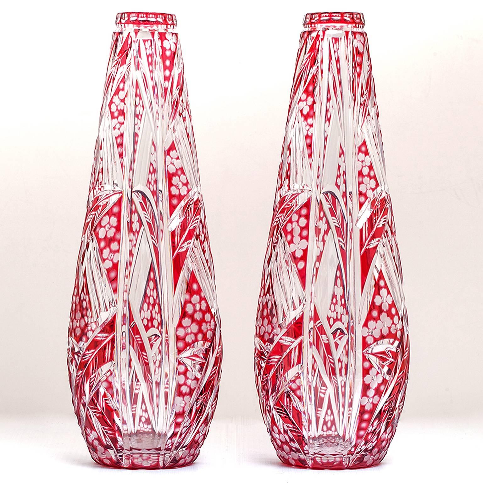 Circa 1930s, by Saint Louis, France.  This incredible pair of Art Deco vases by Saint Louis flaunts a sleek floral pattern in ruby cut-to-clear crystal. Exciting to look at, the design has more than one visual surface.  At the fine detail level,