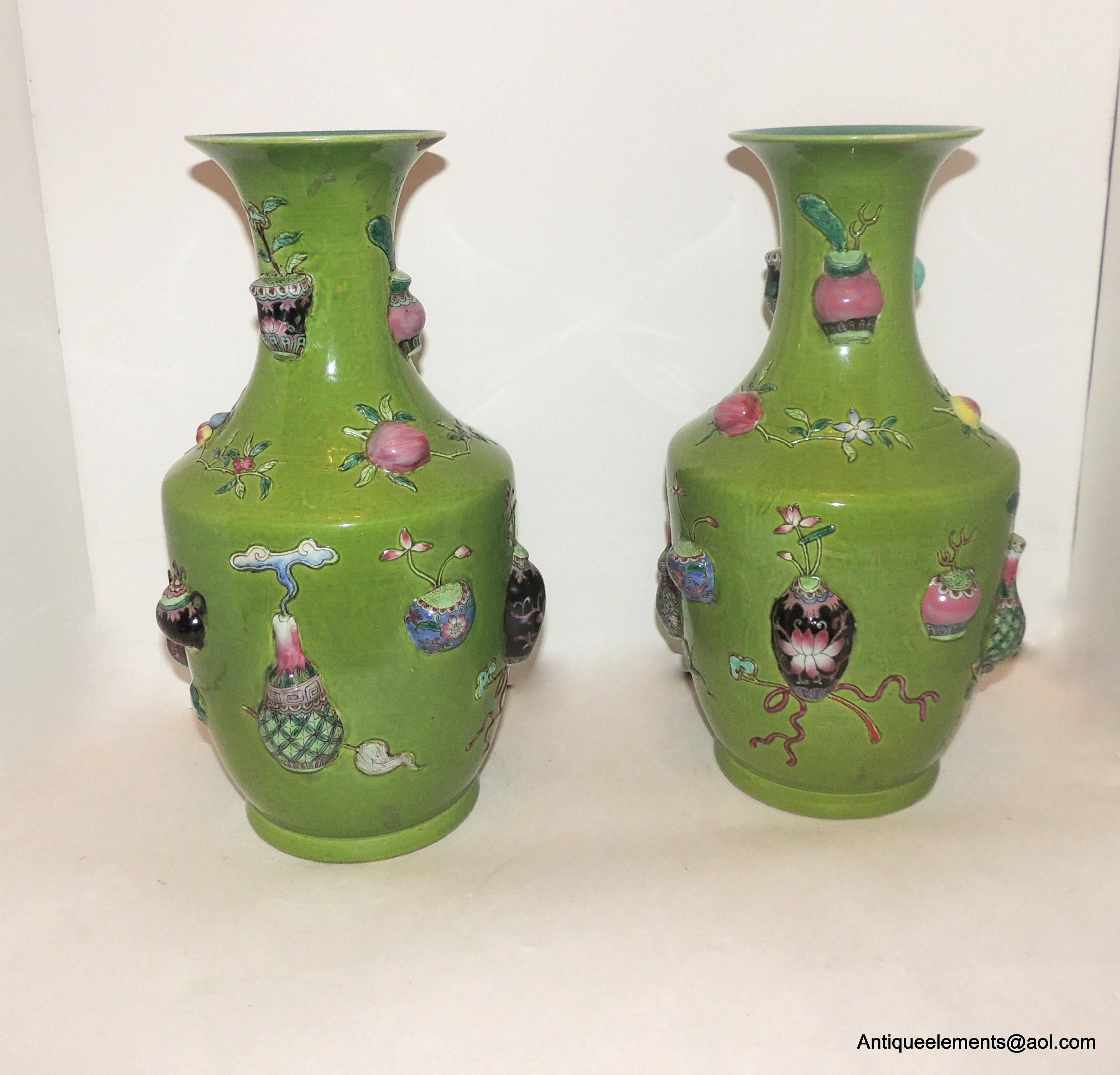 A fine pair of Chinese rotating shaped vases decorated with relief molded precious urn and floral objects in bright shades of magenta, teal green, and pinks on a bright green ground. Each measures 14
