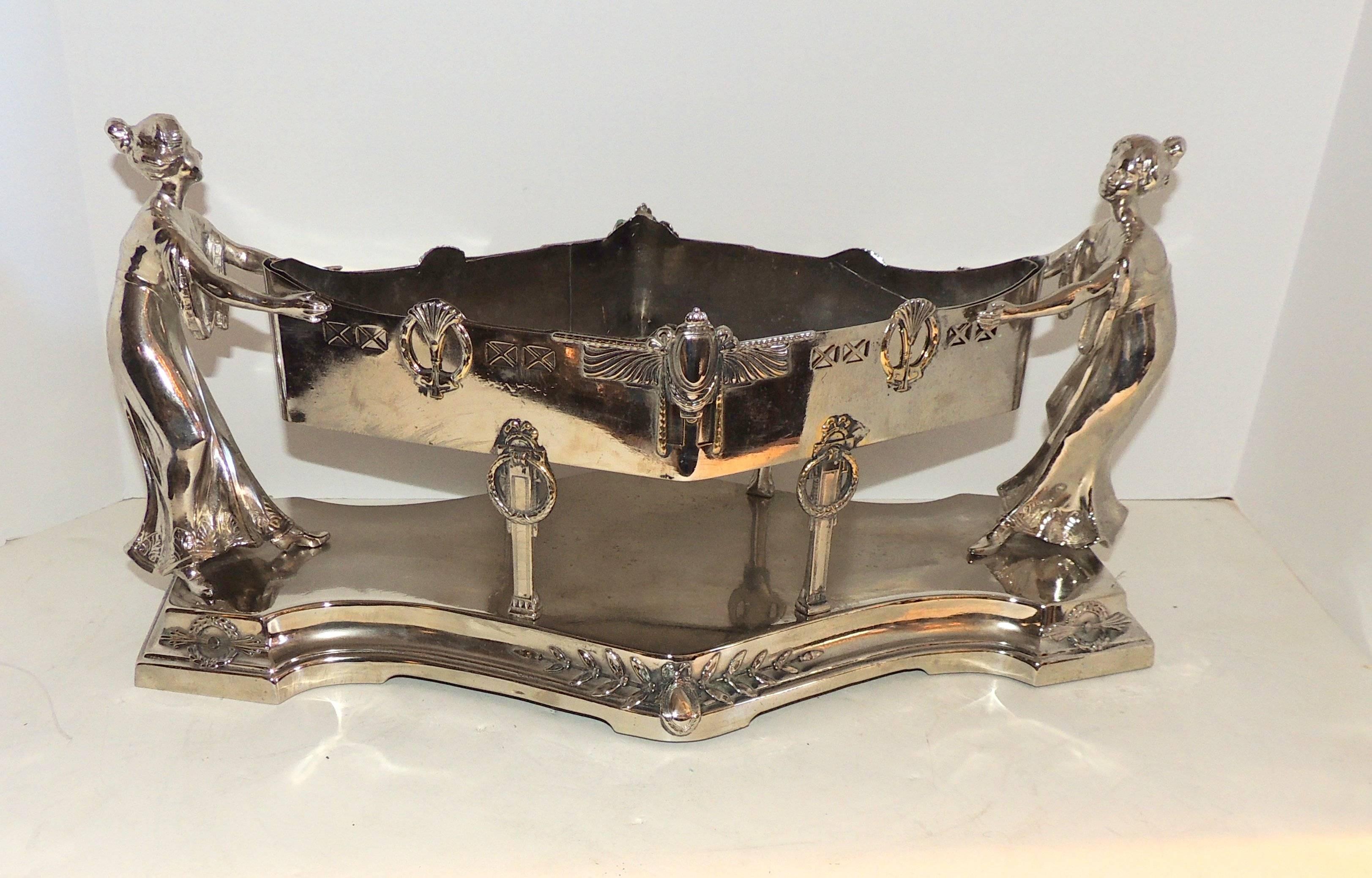 A wonderful silver plated Art Deco centerpiece with two female figures supporting the diamond shape centerpiece with removable insert. Decorated with draping, wreaths and filigree detail.

Measures: 18