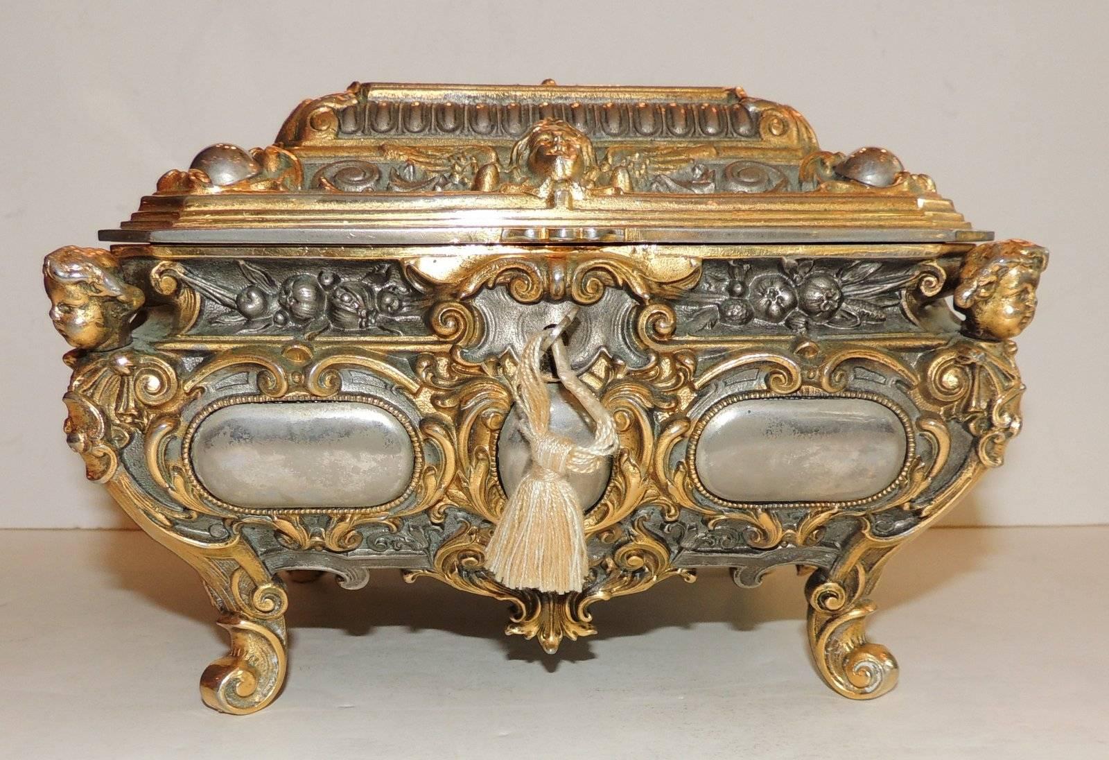 A very ornate rectangular casket with rich cherub ormolu corner mounts with scroll feet, floral bouquets and a winged cherub mask escutcheon on top the hinged cover. Silver medallions surround the corners of the box and rich blue velvet lines the