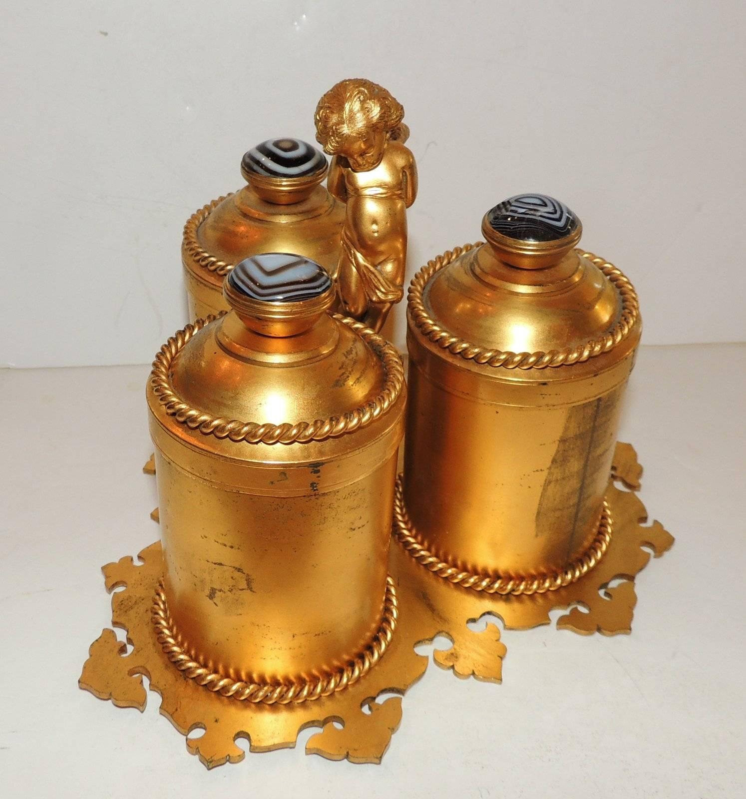 Beautiful Agates decorate the tops of this unusual vanity perfume set. Each of the three perfume holders is decorated with rope trim as are the tops. The interior of the bronze tops are lined with purple velvet as is the bottom. Each of the lovely