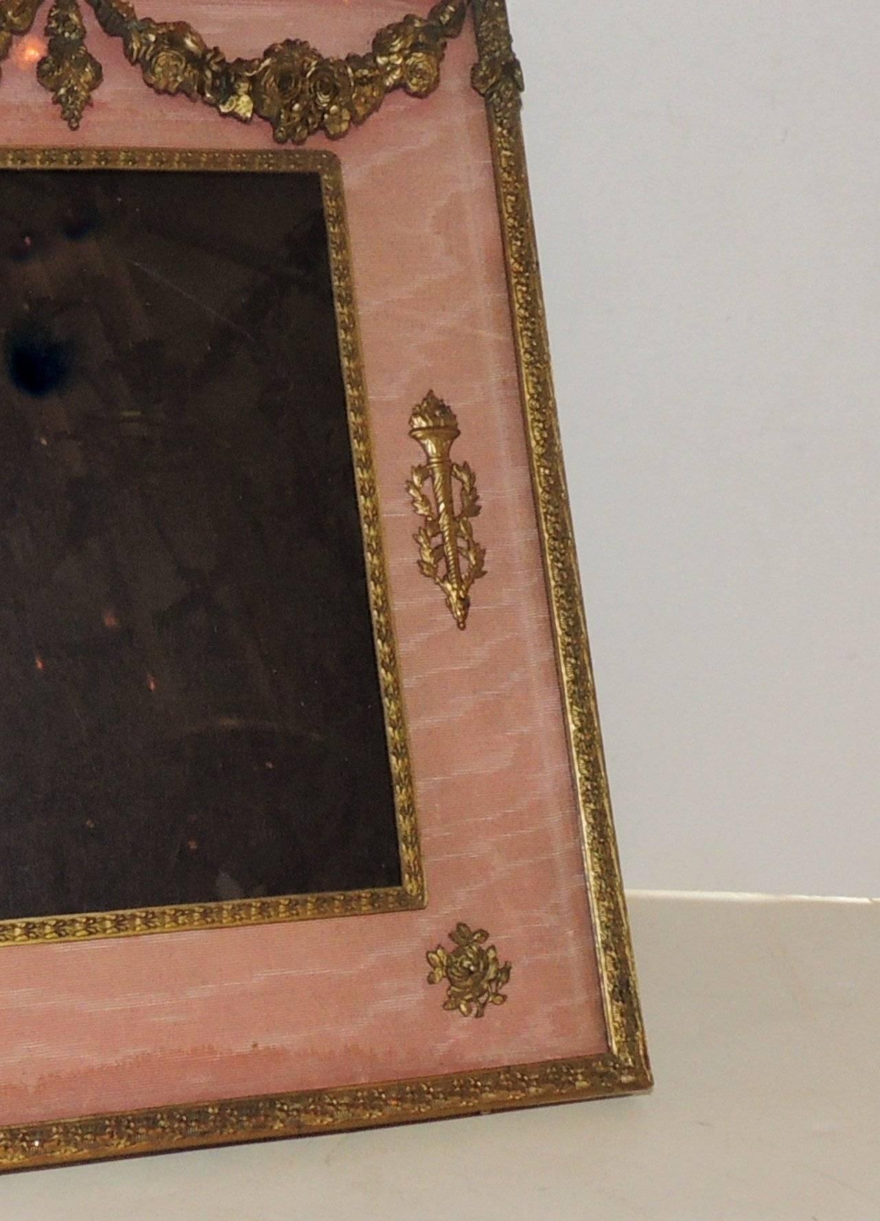 Beautifully aged Empire style doré bronze picture frame with pink silk accented with draped roses and filigree and bow with wreath spray.

Measures: 10.5